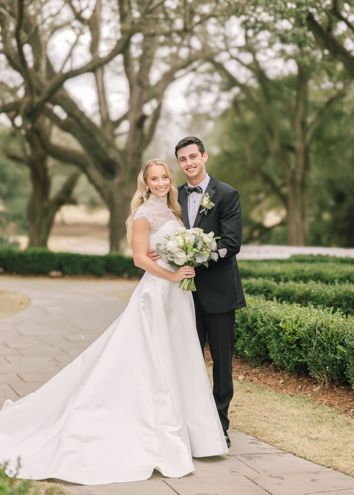 A newlywed couple shares an intimate moment on a garden path surrounded by lush greenery.