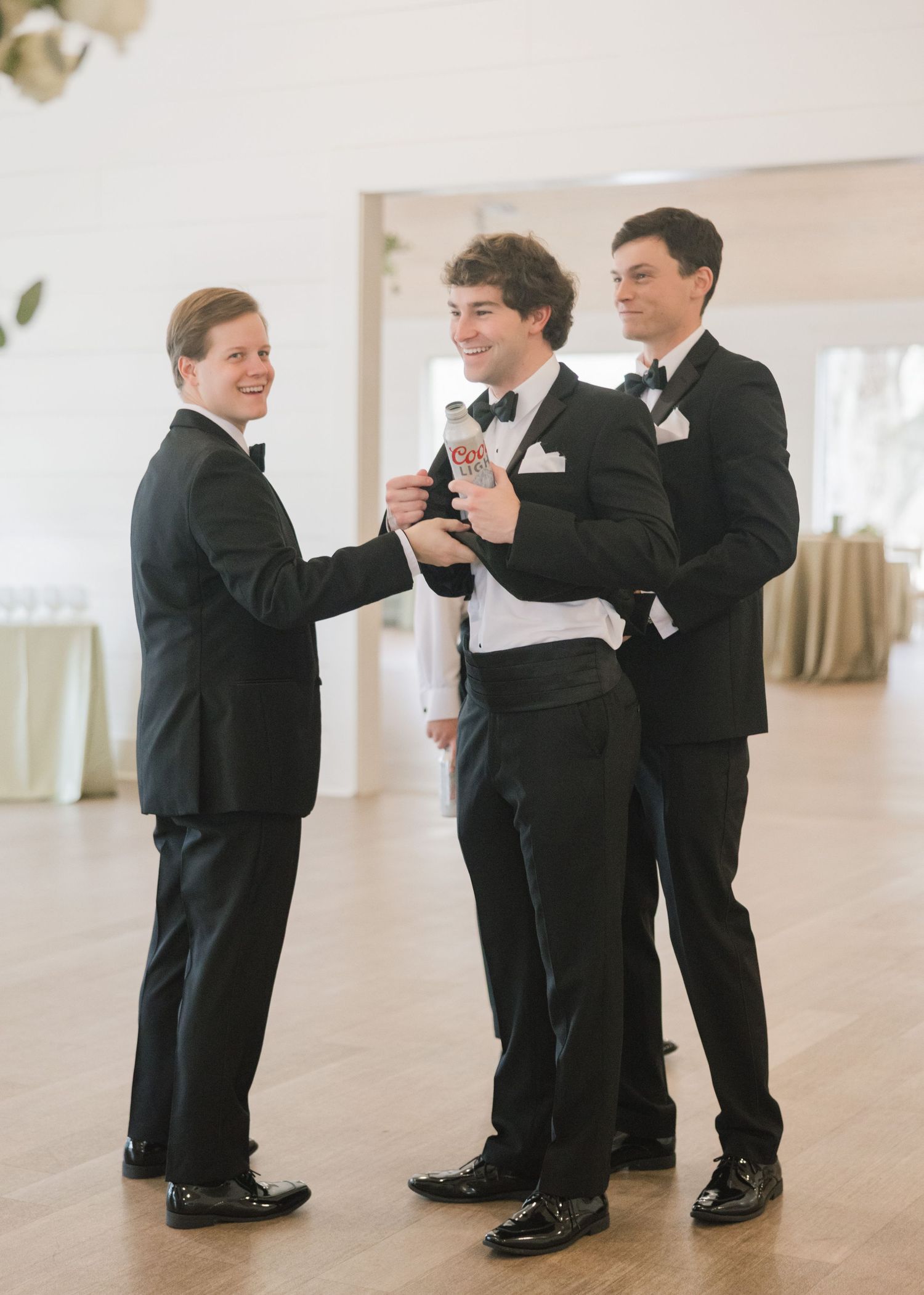 A sequence of photos showing groomsmen teaching a young boy in a tuxedo how to tie a necktie.
