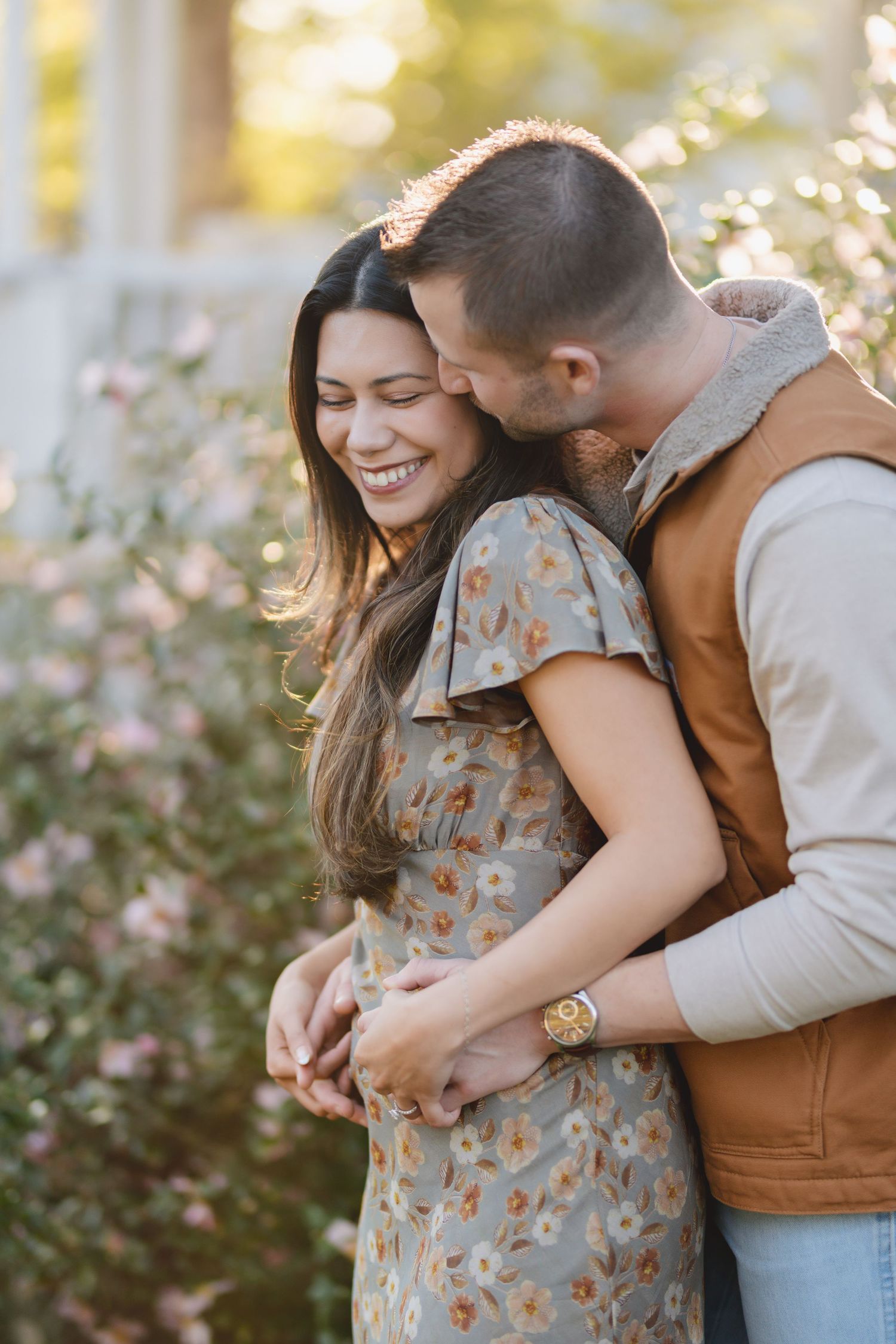 Tender embrace among blooming flowers during golden hour photoshoot.