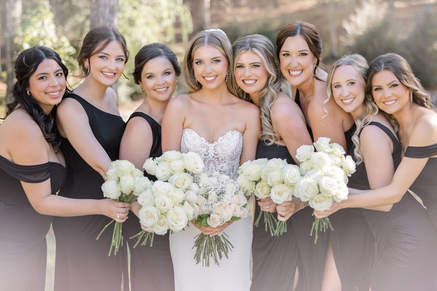 Bridal party in black dresses pose with white hydrangea bouquets during elegant outdoor wedding photo shoot.