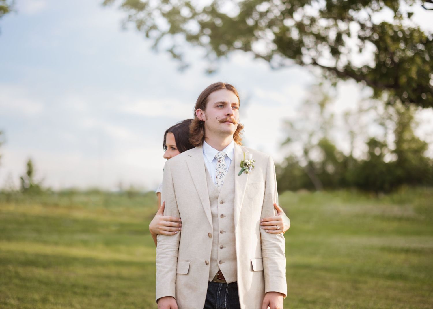 Couple sharing intimate first look moment in white attire against natural outdoor setting.