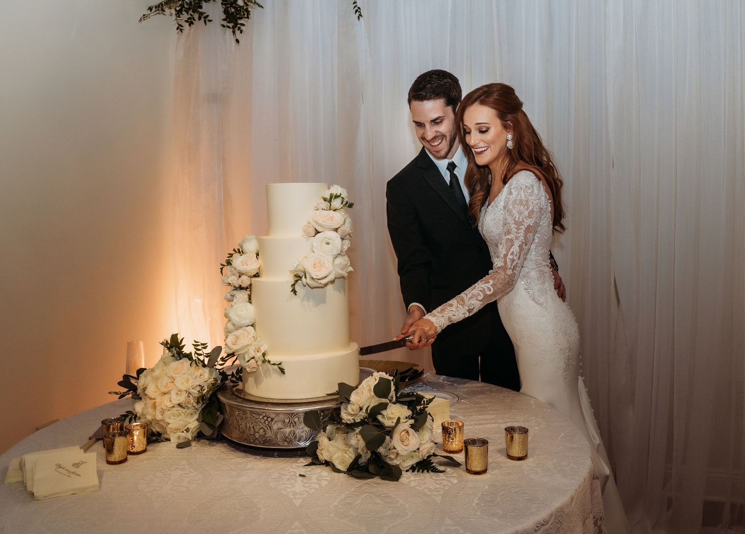 Newlyweds cutting their elegant white wedding cake together at reception.