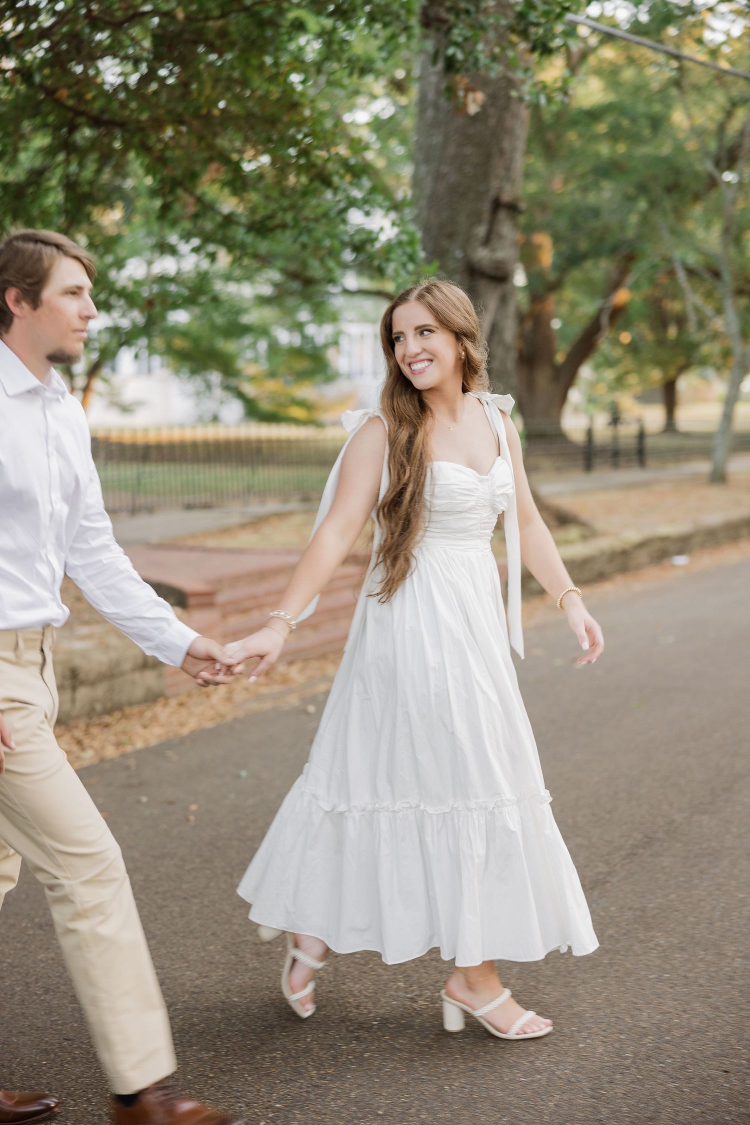 Couple dancing together on tree-lined path in elegant attire.
