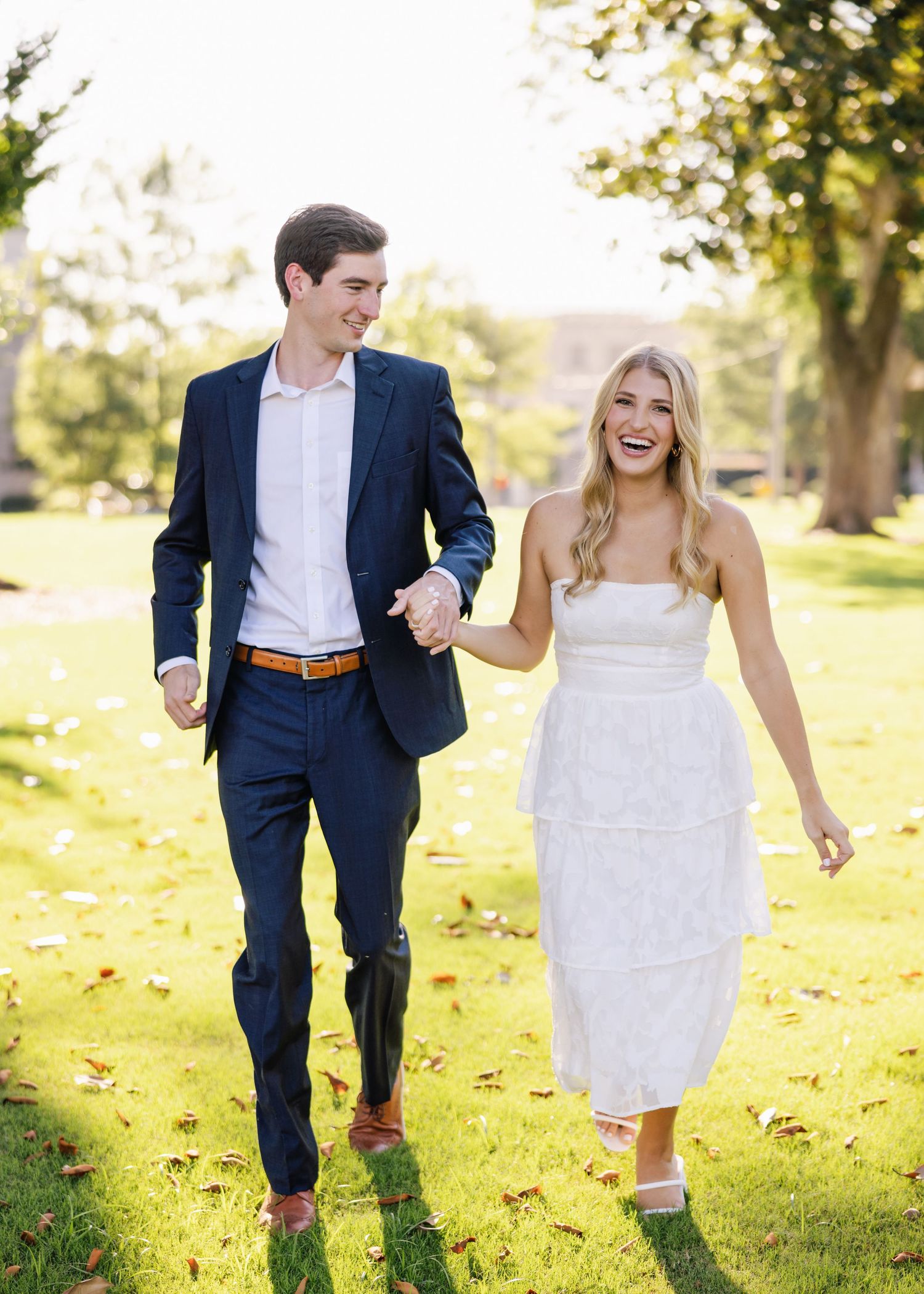 Happy couple walking together on grass, him in navy suit and her in white sundress.