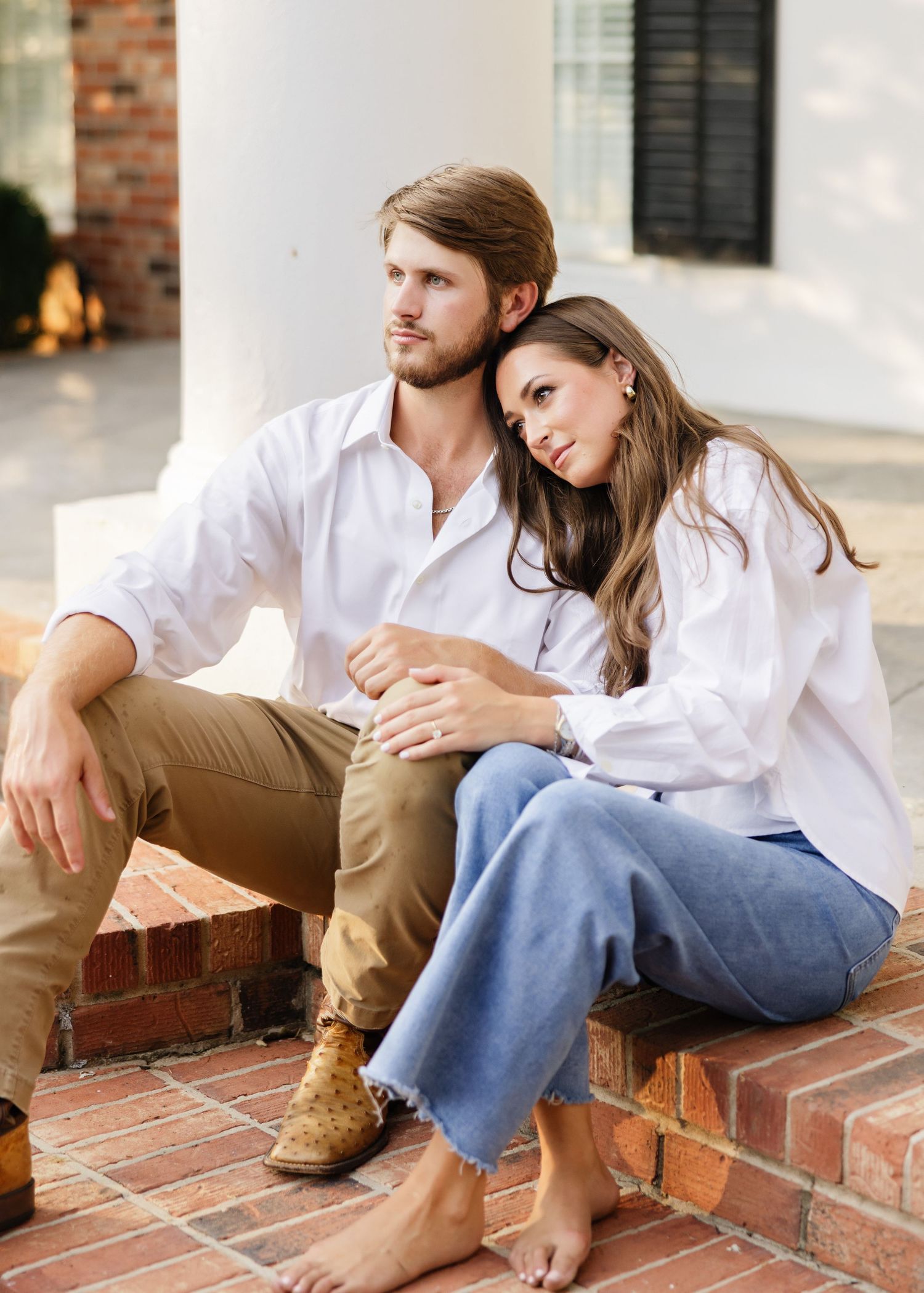 Couple relaxing on brick steps sharing intimate moments in casual white and khaki outfits.