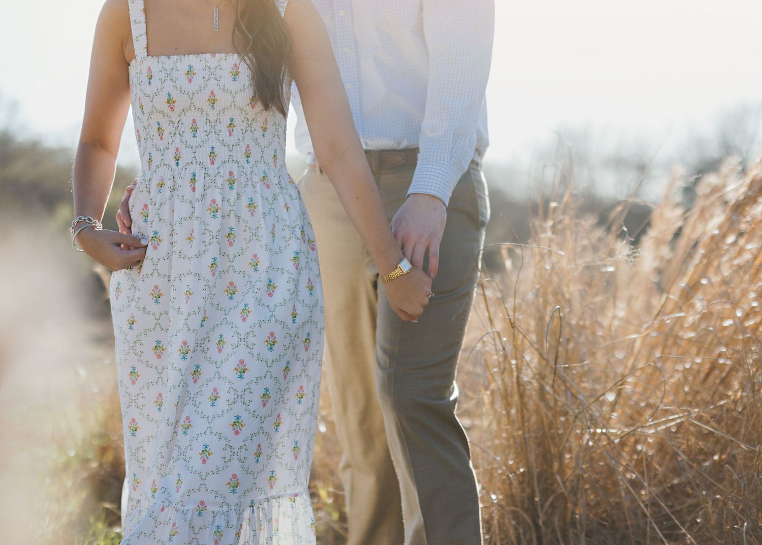 Couple holding hands in golden field during sunset.