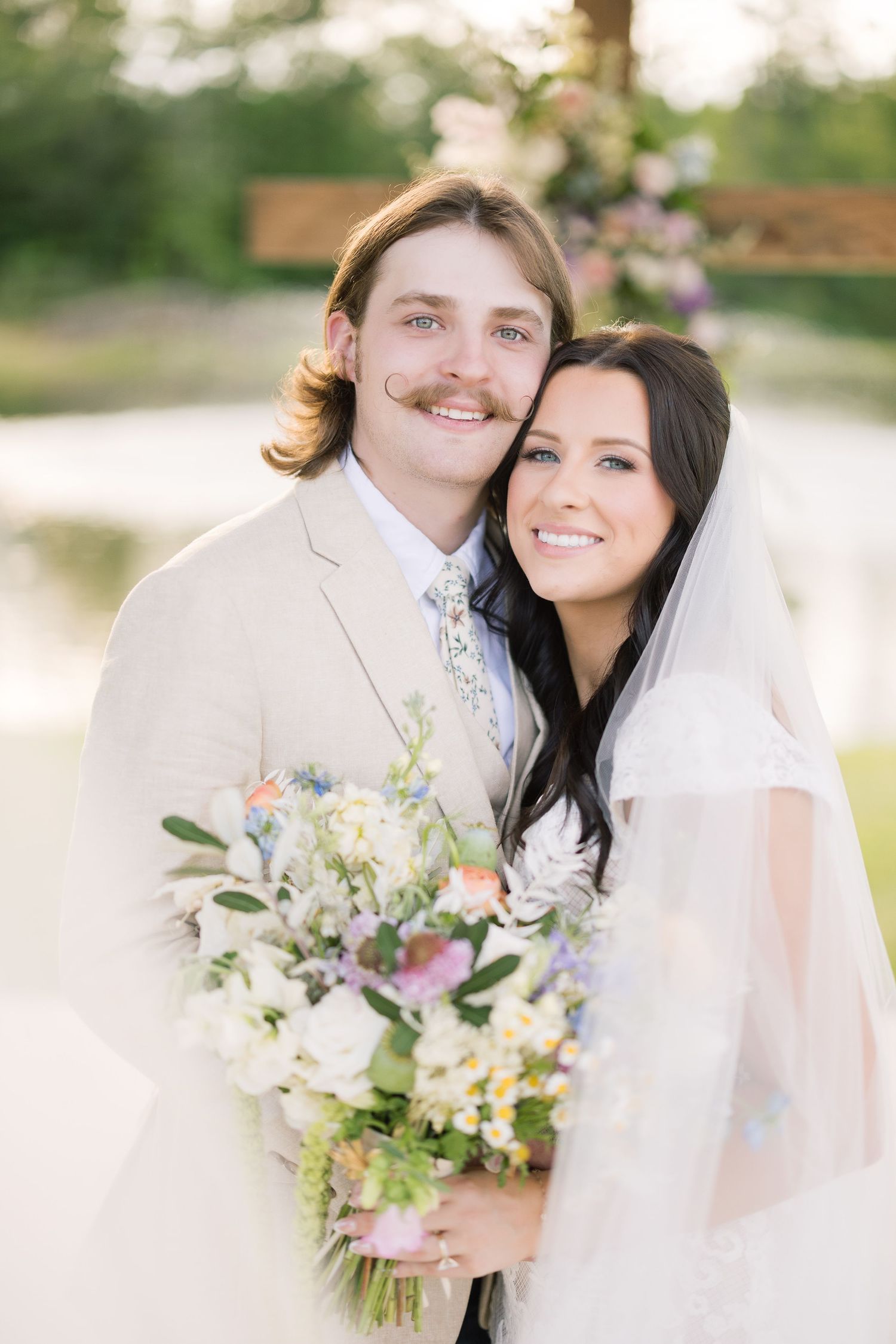 Newlywed couple smiling with colorful wildflower bouquet against garden backdrop.