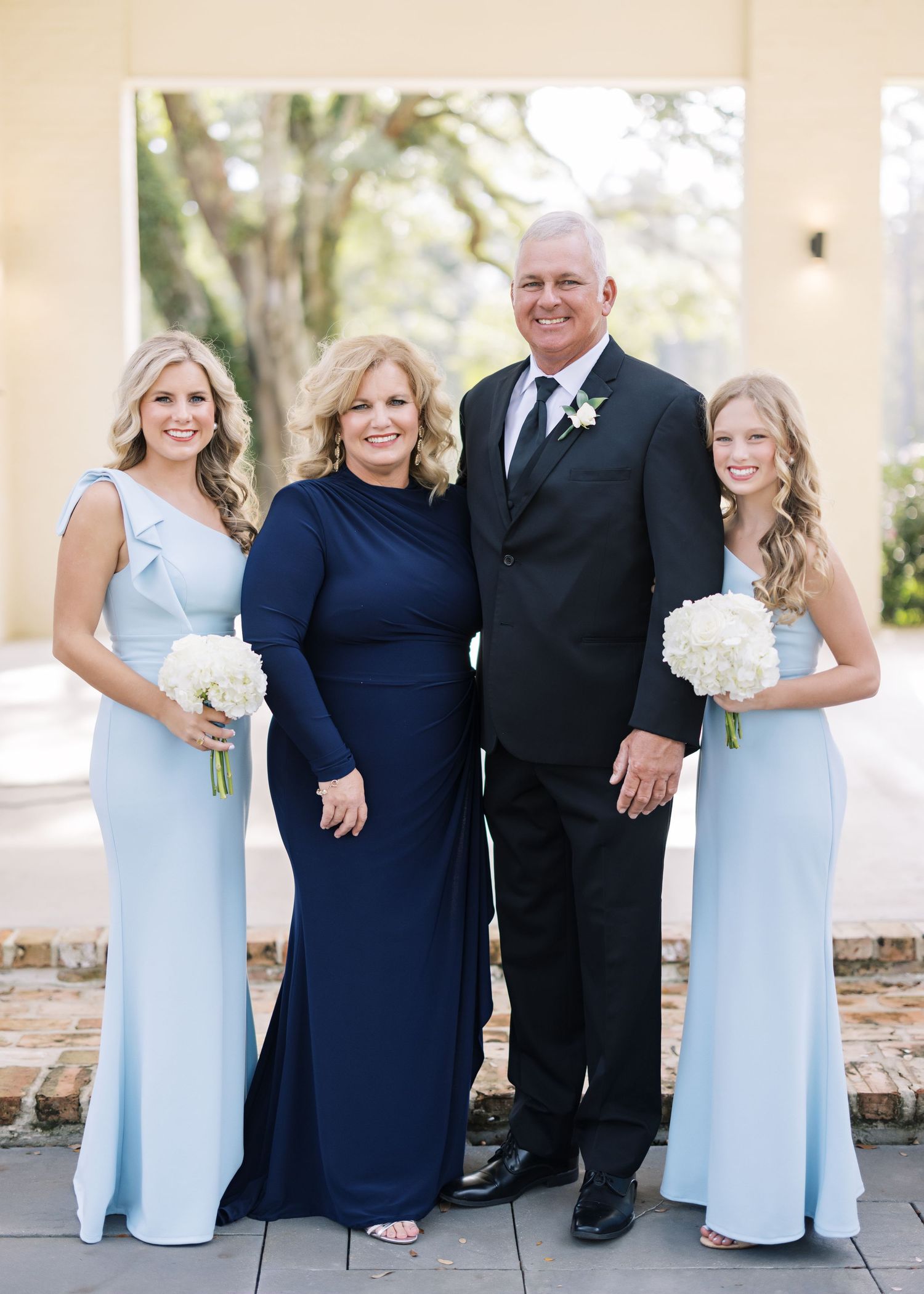 Wedding party in light blue dresses and navy attire poses together on porch.