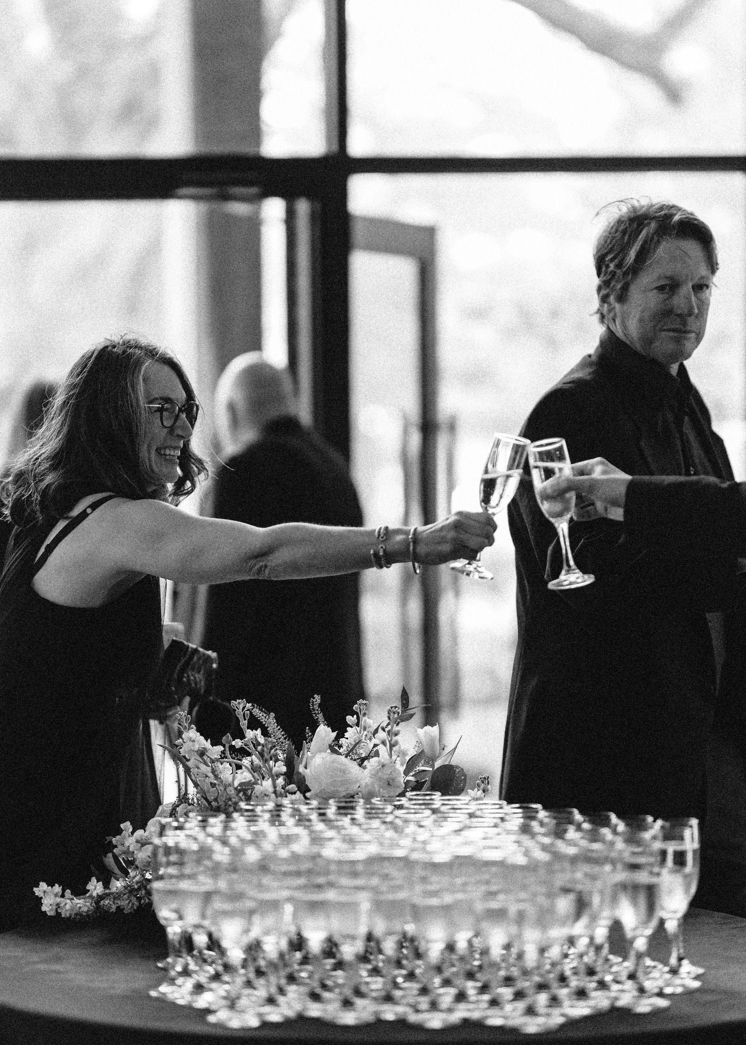People reach for champagne flutes from an elegant tower display at formal event.