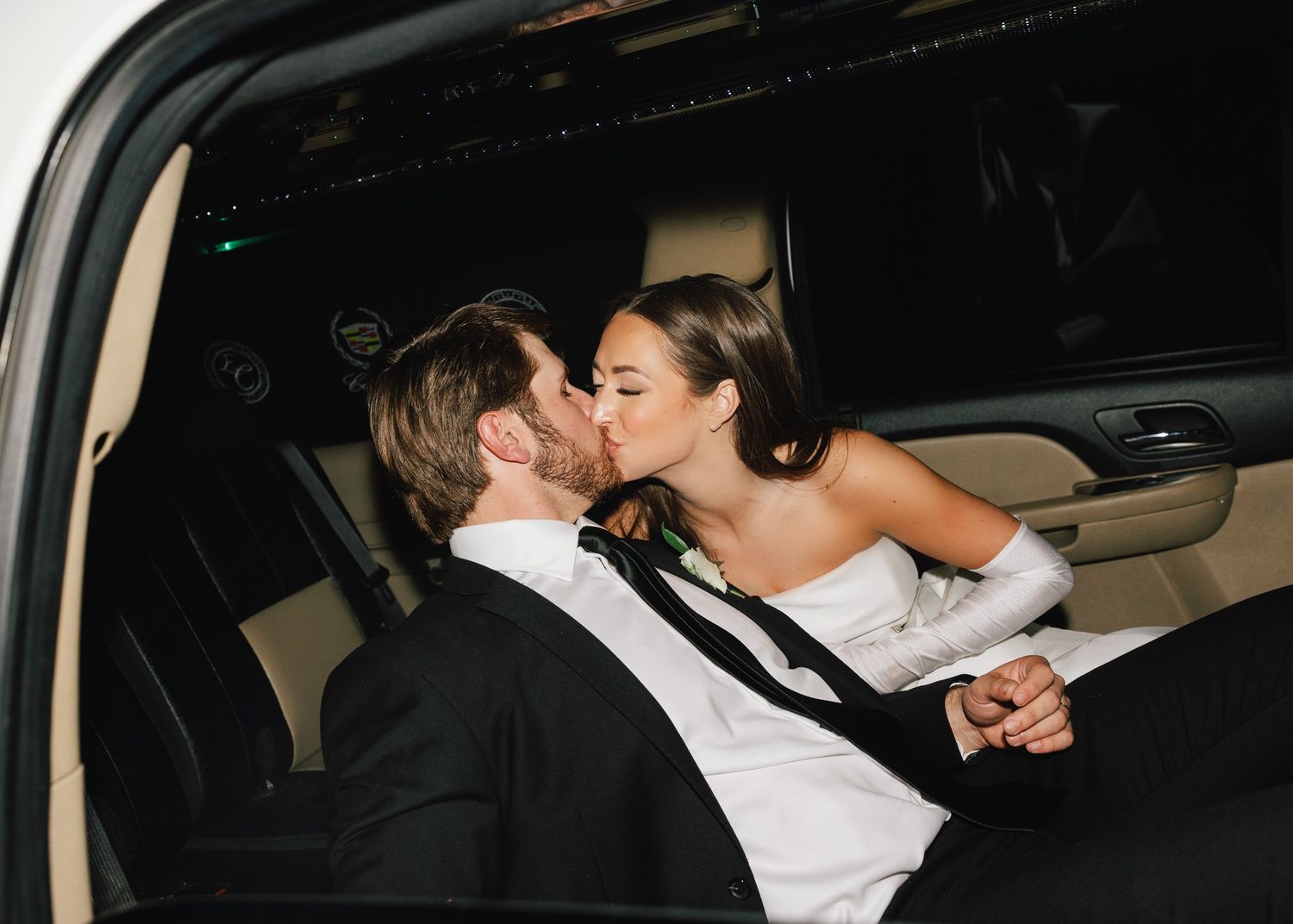 A couple in formal attire share an intimate moment in the back seat of a car.
