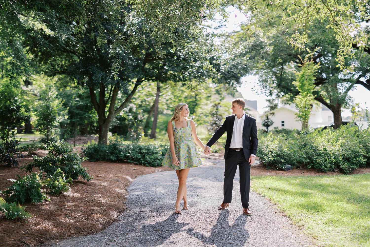Couple walking hand in hand on garden path surrounded by lush trees.