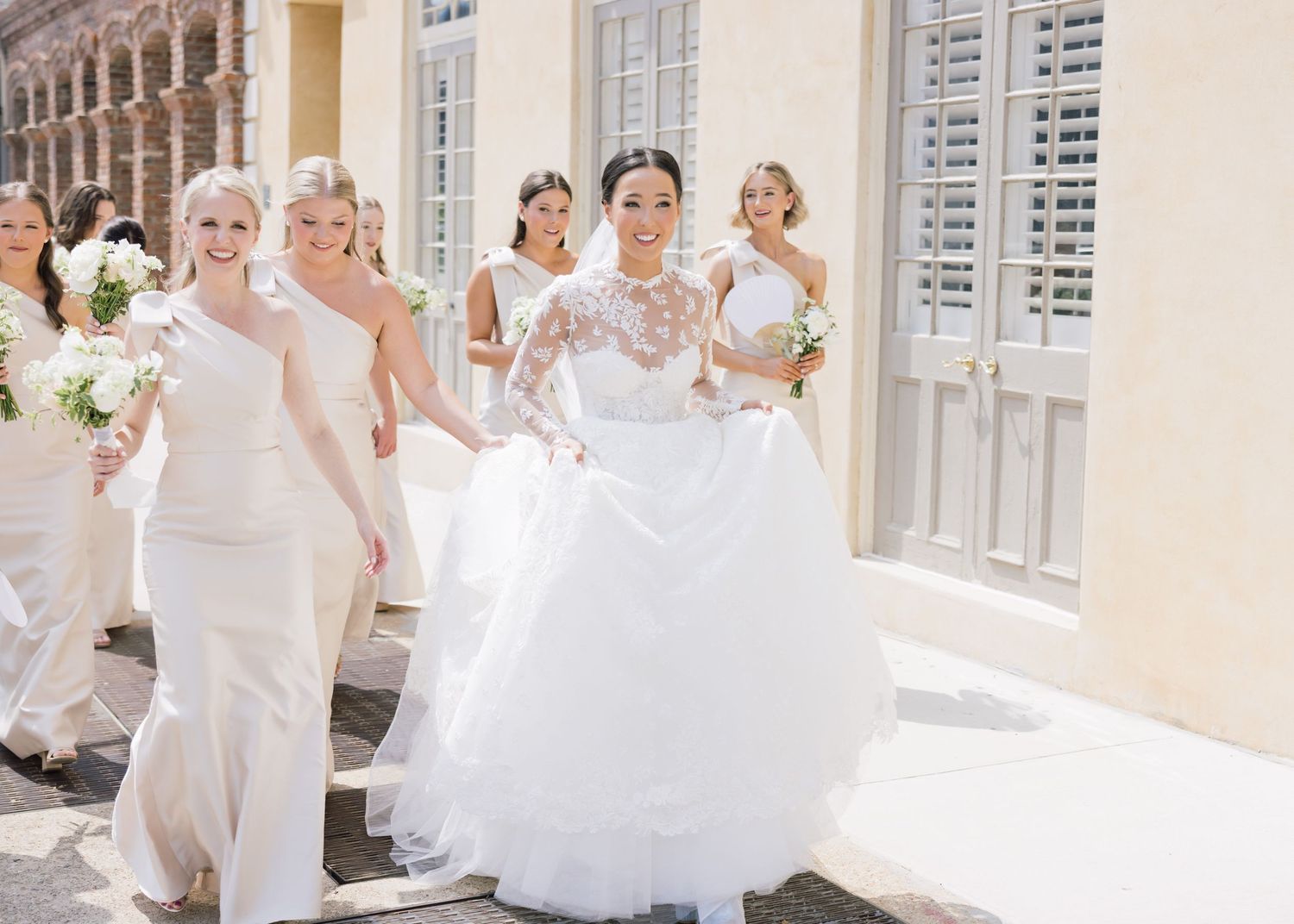 Wedding party walking along a columned building with bridesmaids in white dresses.