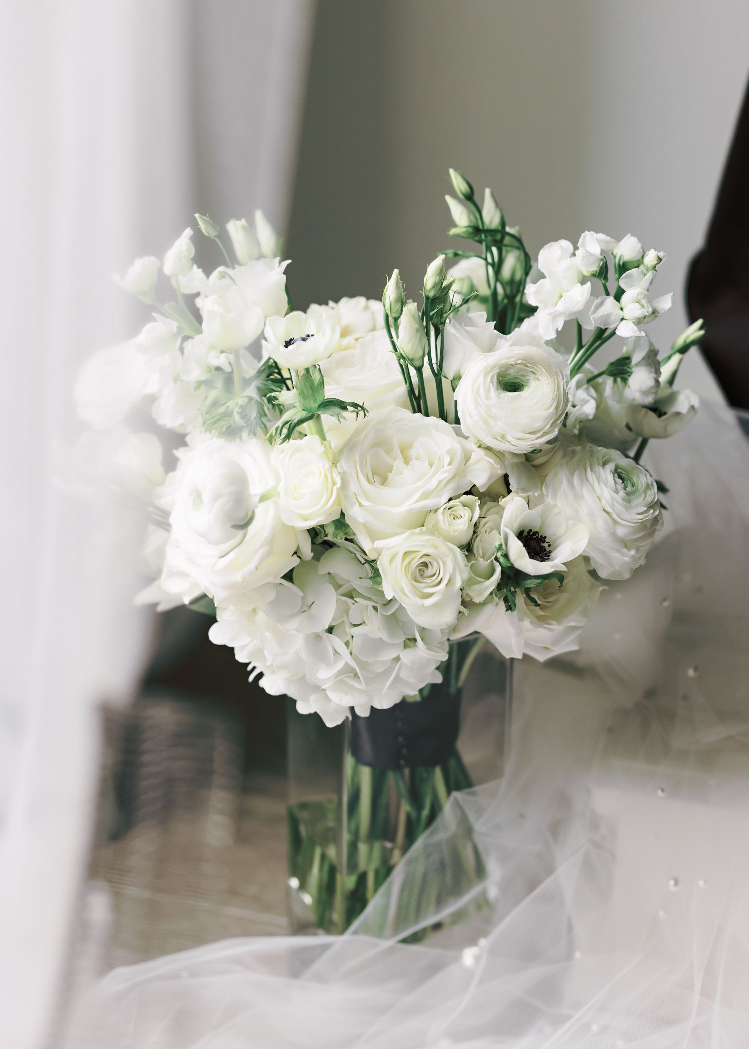 Elegant white rose and ranunculus bridal bouquet with greenery against light background.