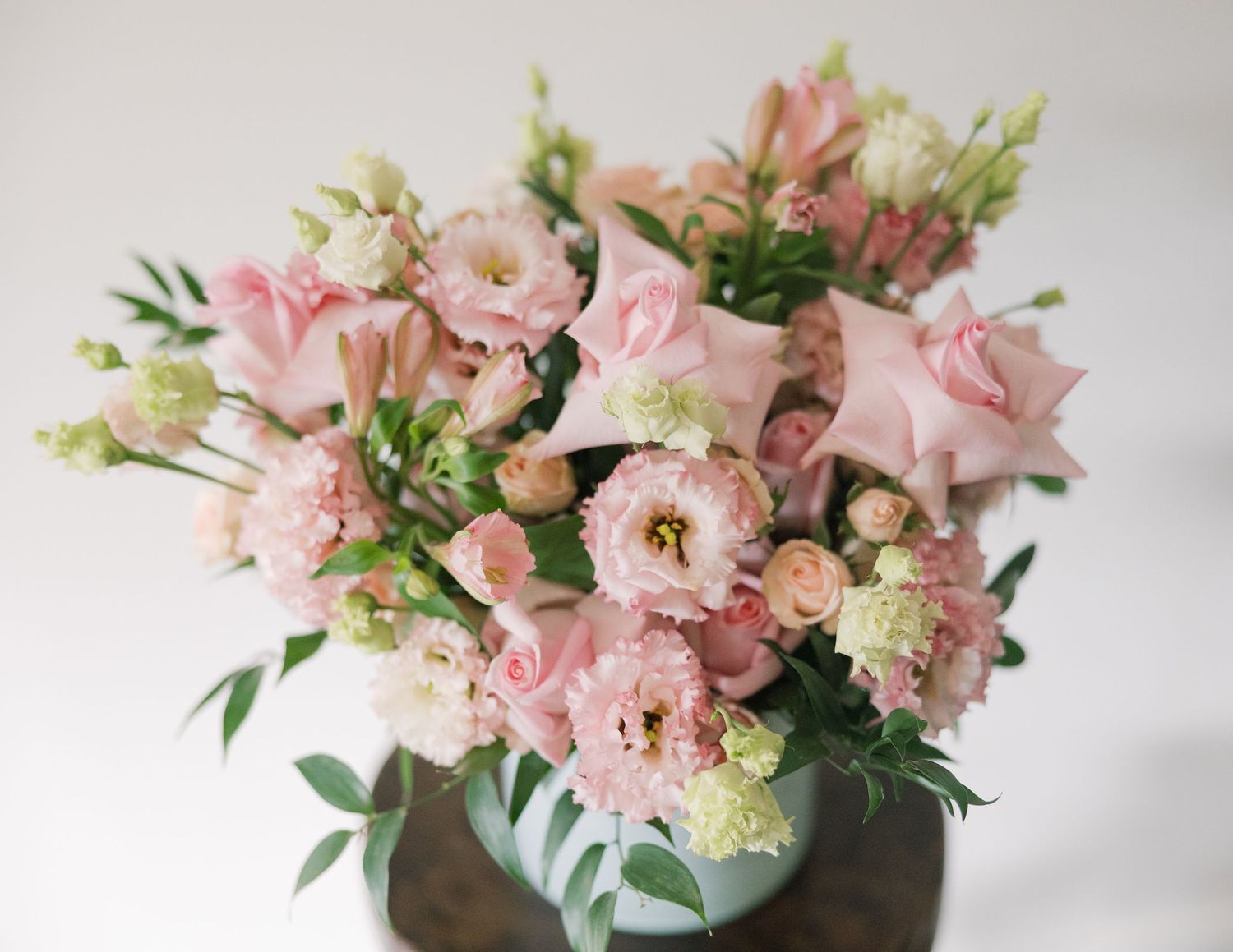 A series of pink and blush floral arrangements in metallic vases against a light background.