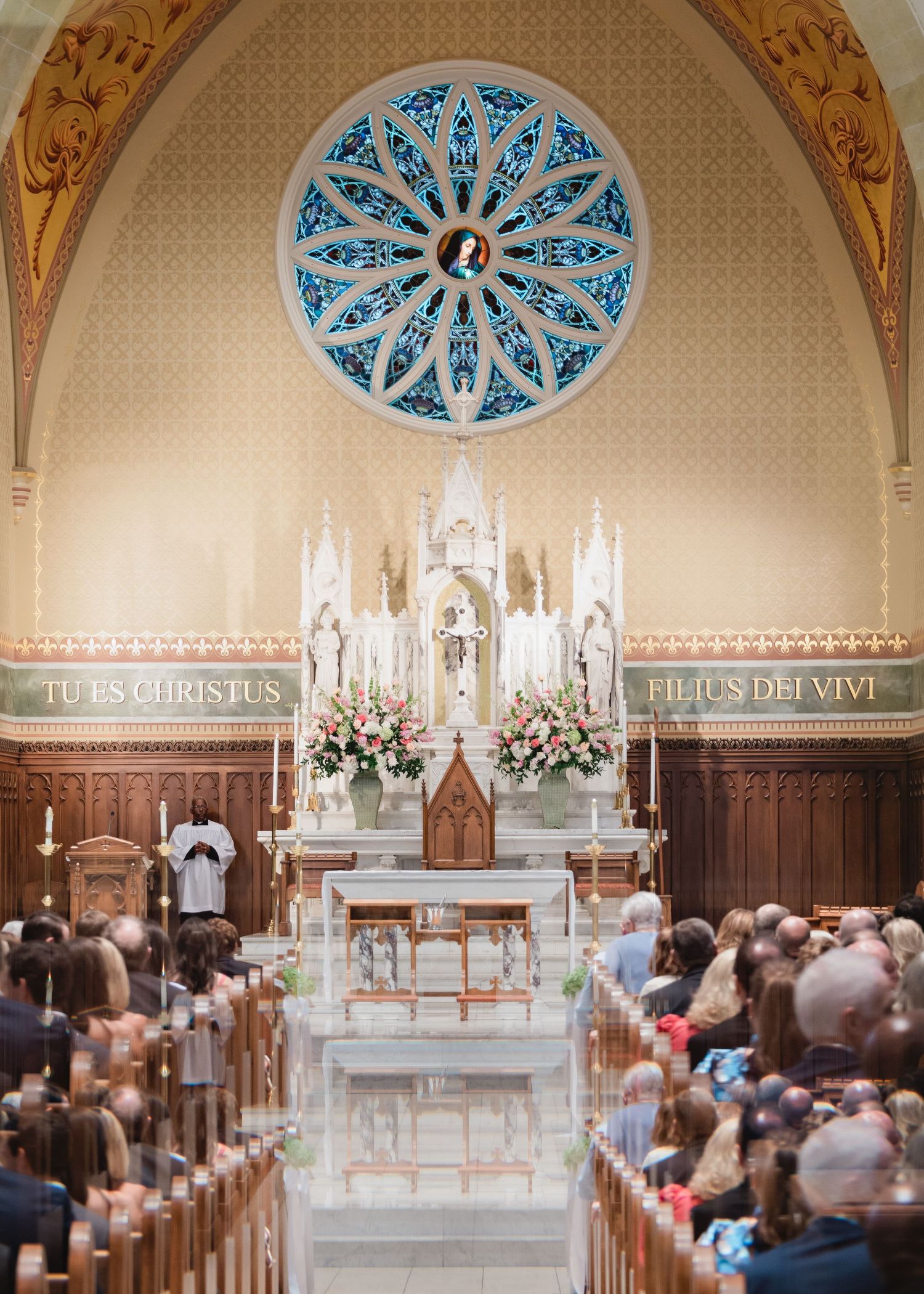 Interior panorama of a historic church sanctuary with ornate arches, blue rosette windows and traditional wooden pews.
