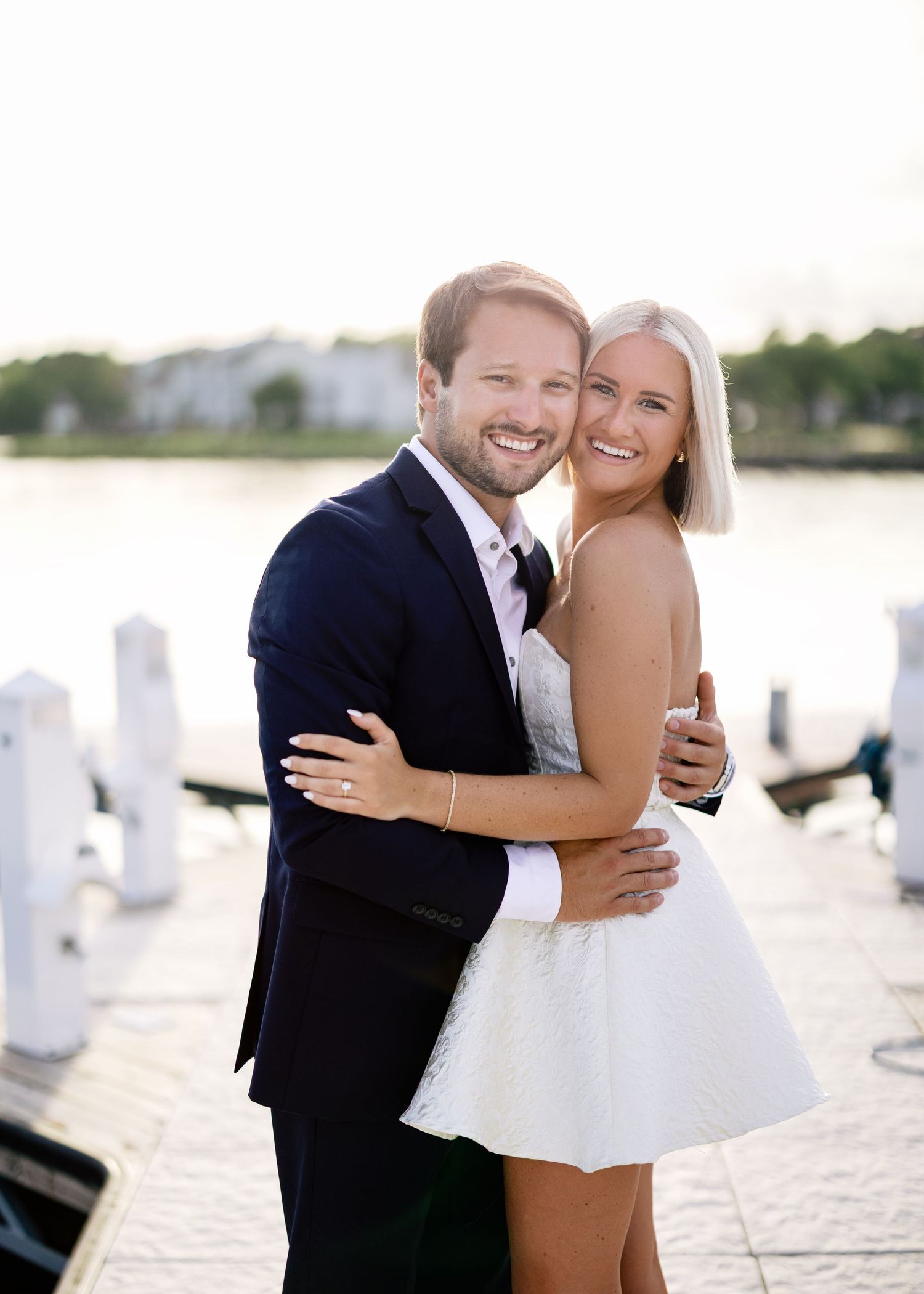 Happy couple sharing joyful moments on waterfront dock in formal attire.