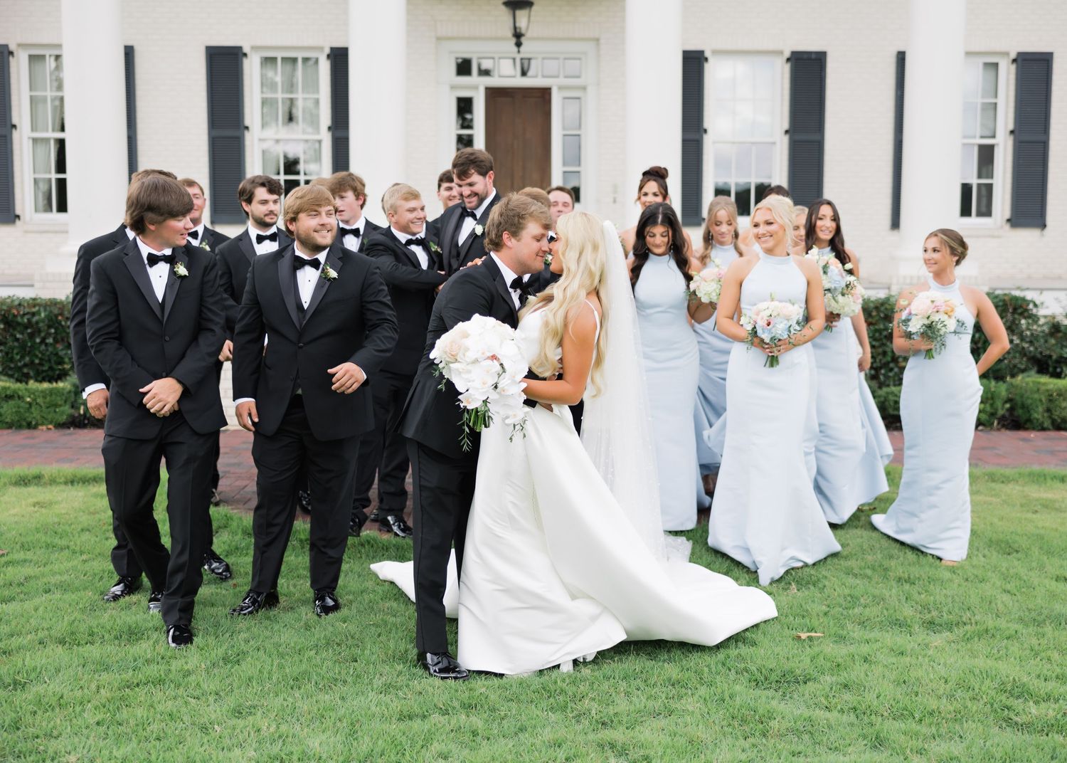 Wedding party poses outdoors on grass while groomsmen lift bride and bridesmaids.