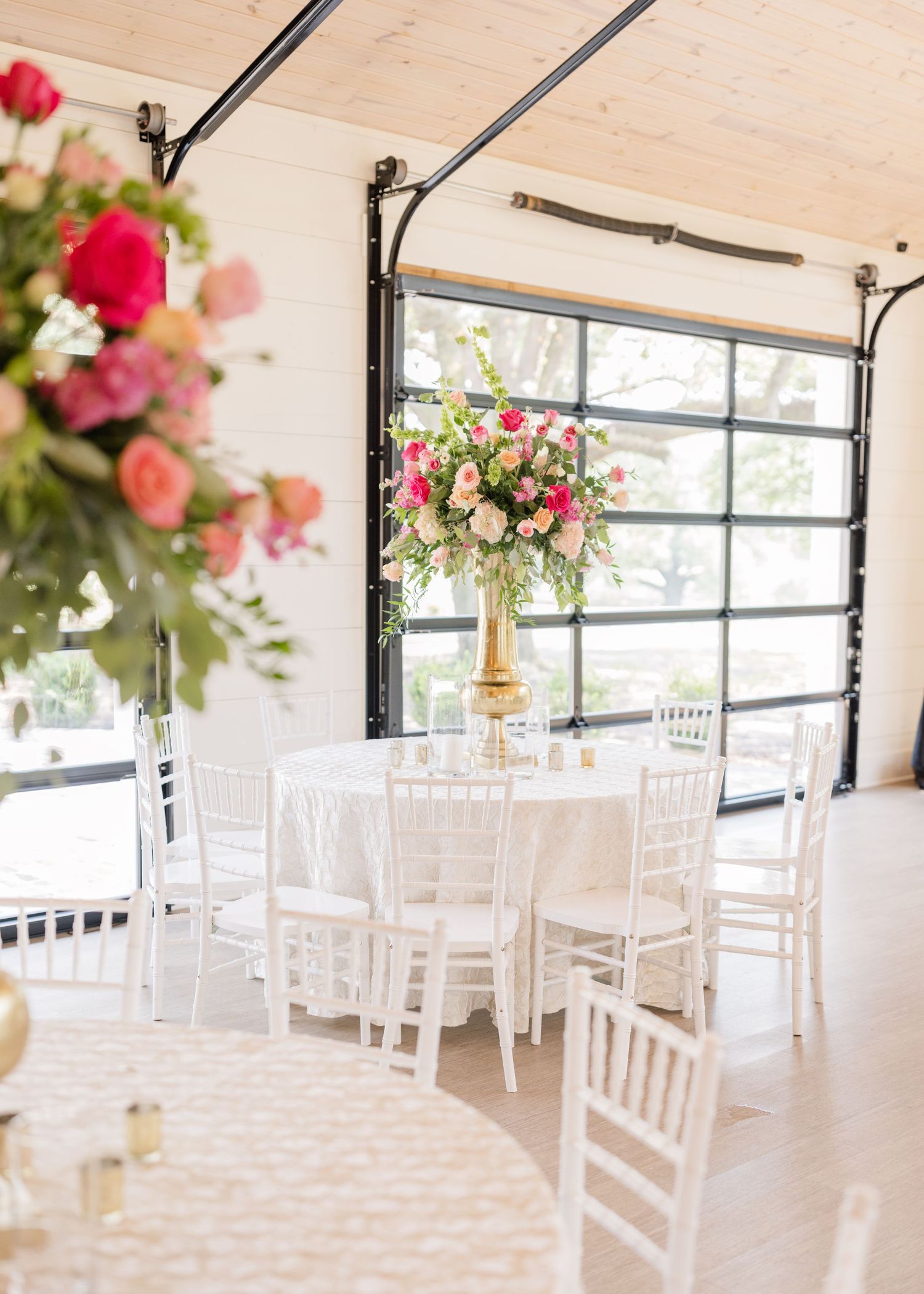 Bright and airy wedding reception venue with white chiavari chairs and pink floral arrangements.
