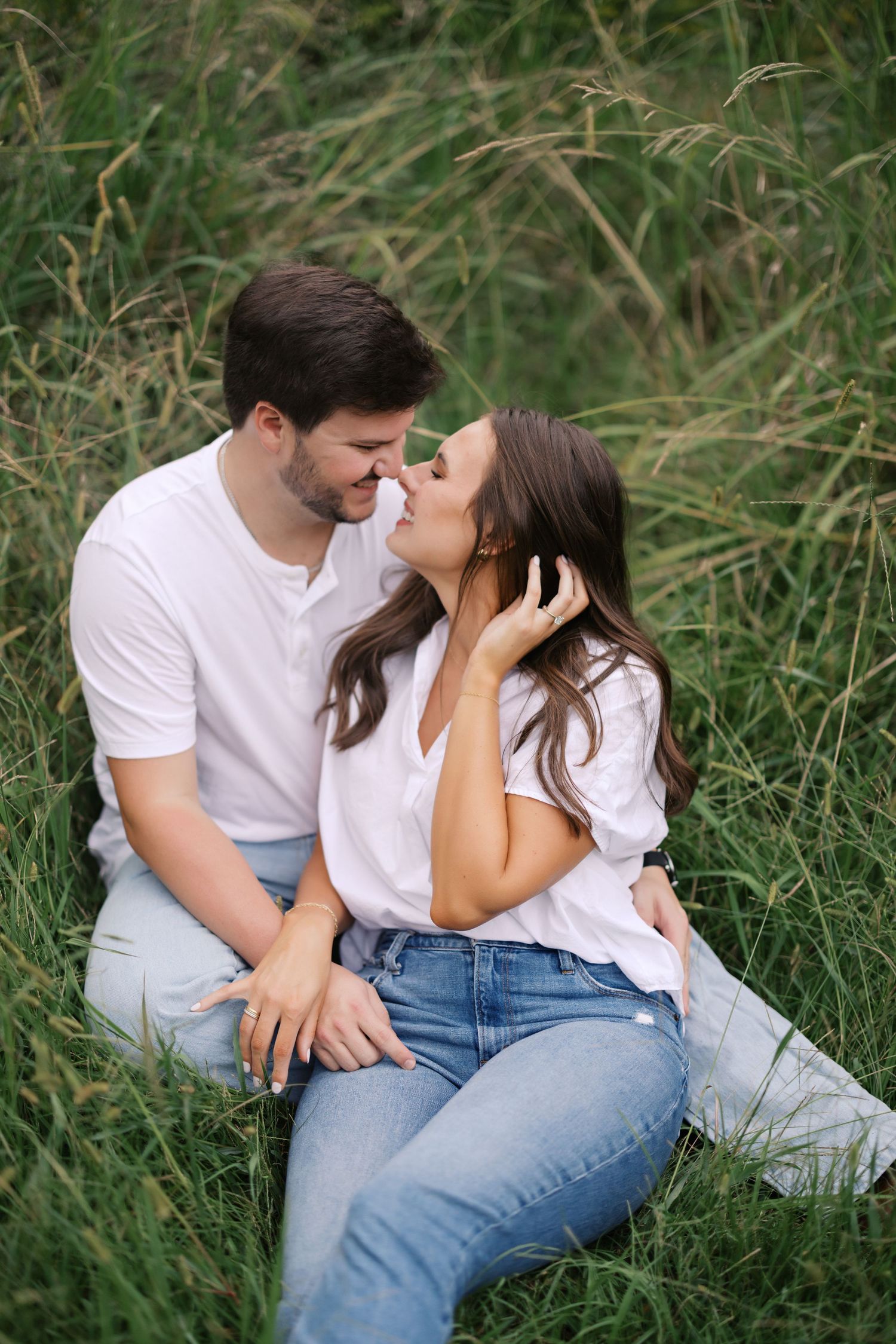 A couple in white shirts and jeans sharing an intimate moment in tall grass.
