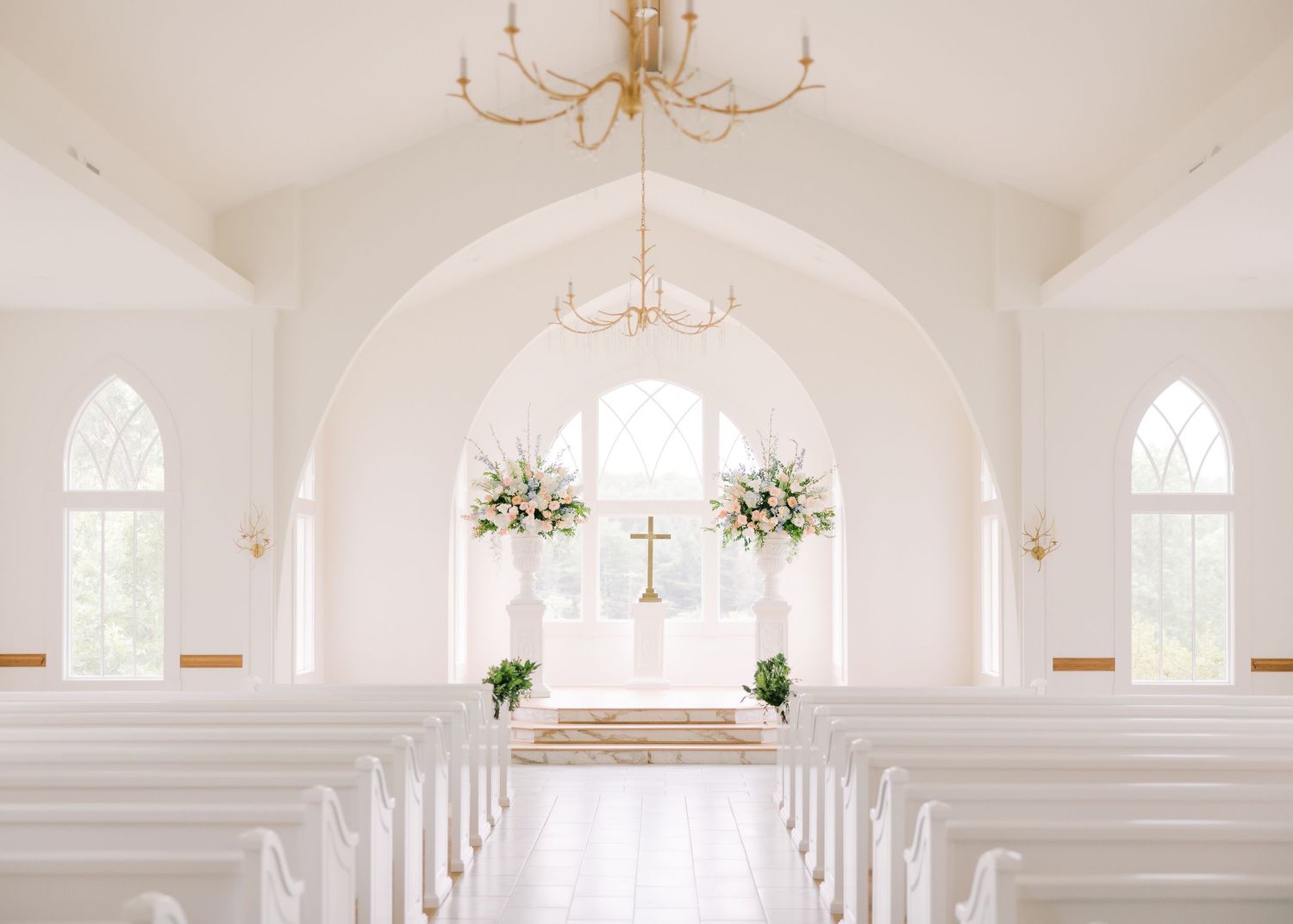 Beautiful white chapel interior with arched windows and chandeliers decorated for a wedding ceremony.