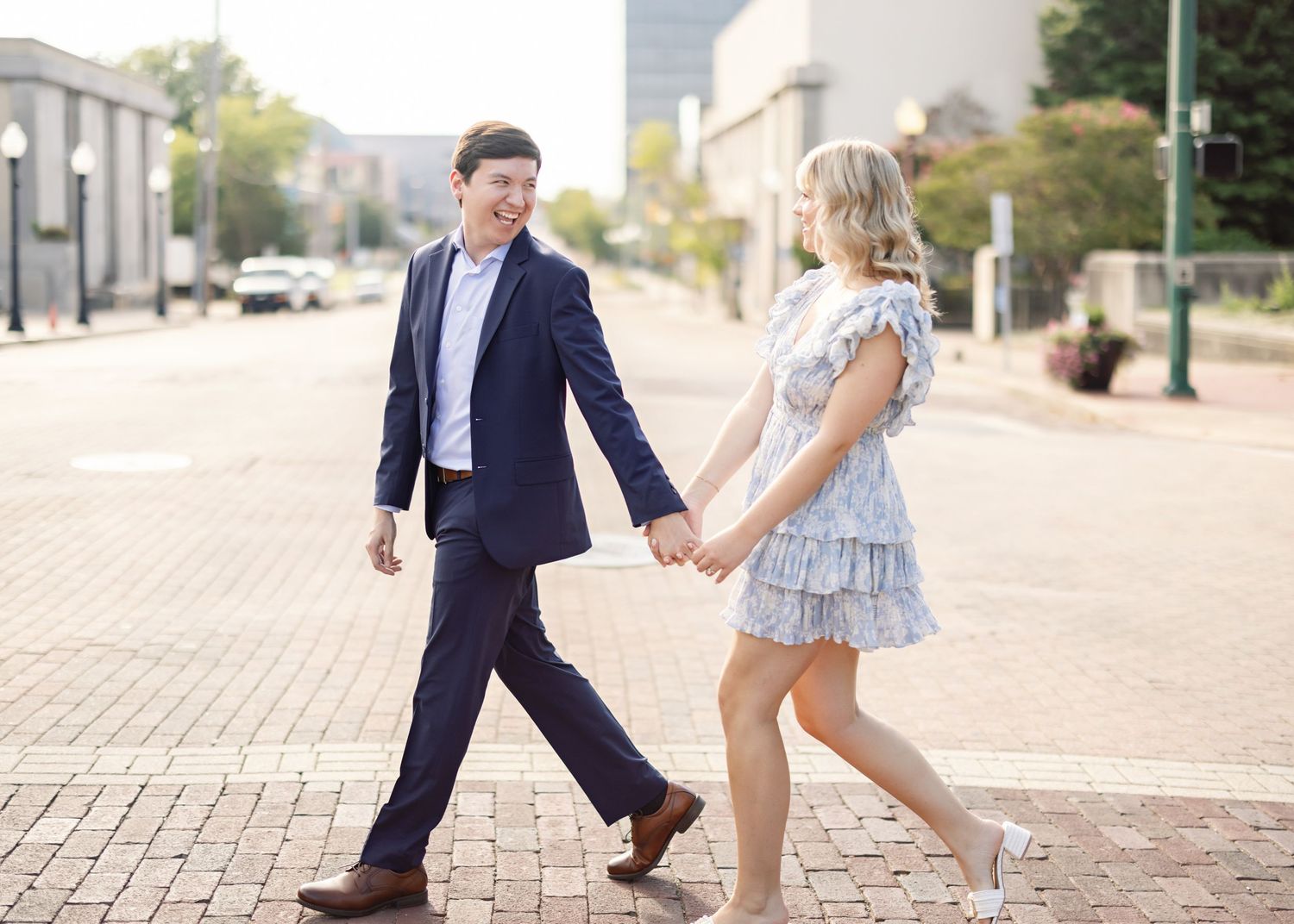 Playful couple dancing on city sidewalk in casual attire.