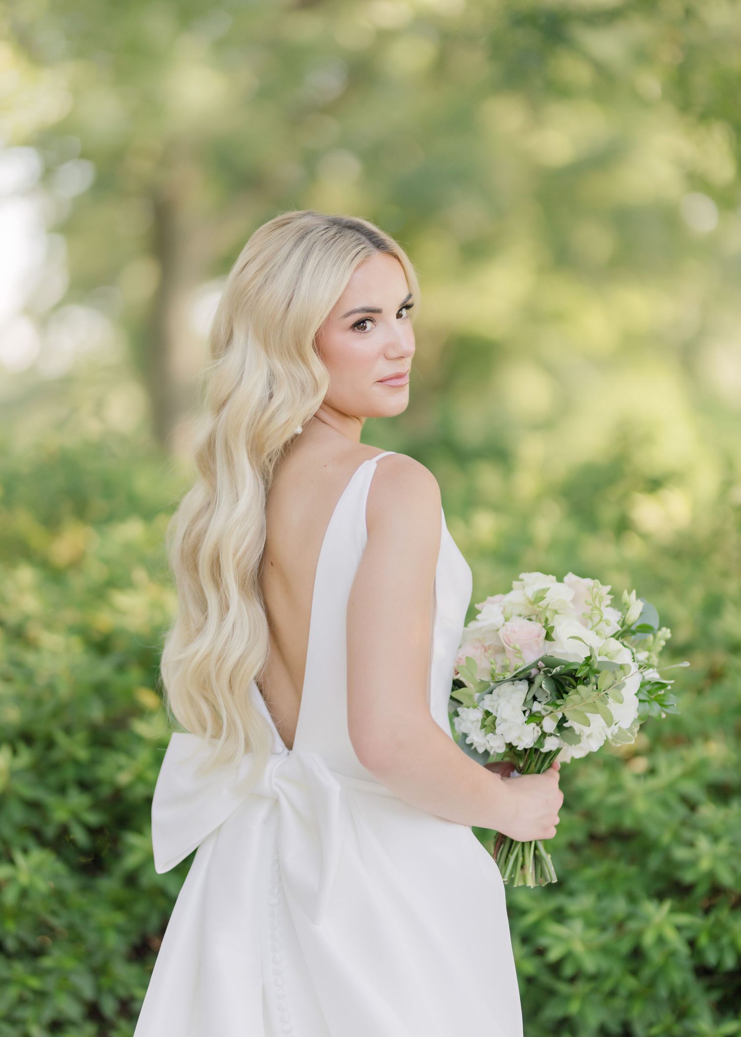 Woman in white dress holds bouquet of white flowers in garden setting.