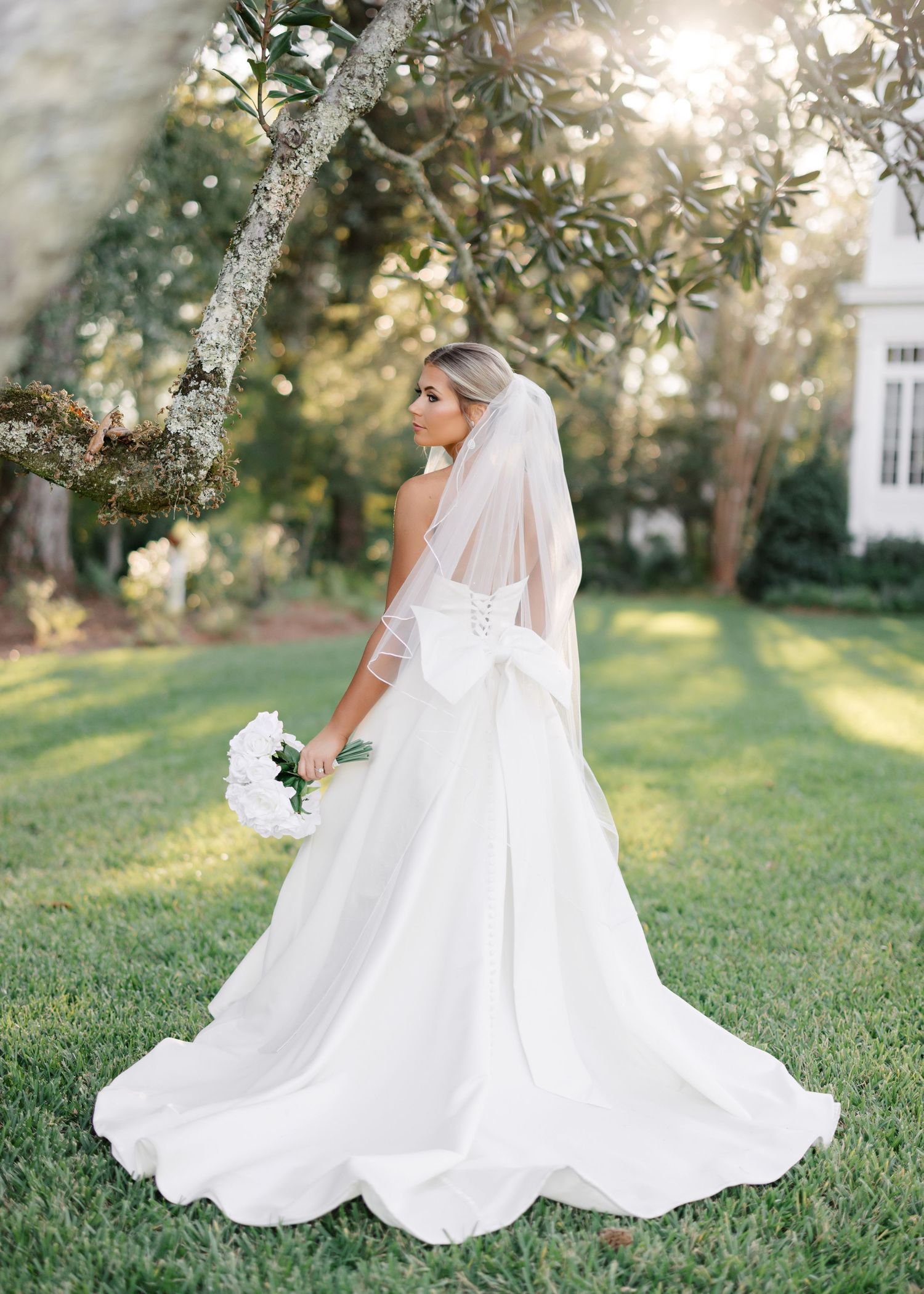 A bride in a flowing white wedding dress twirls gracefully on a sunlit lawn creating a beautiful circular motion.