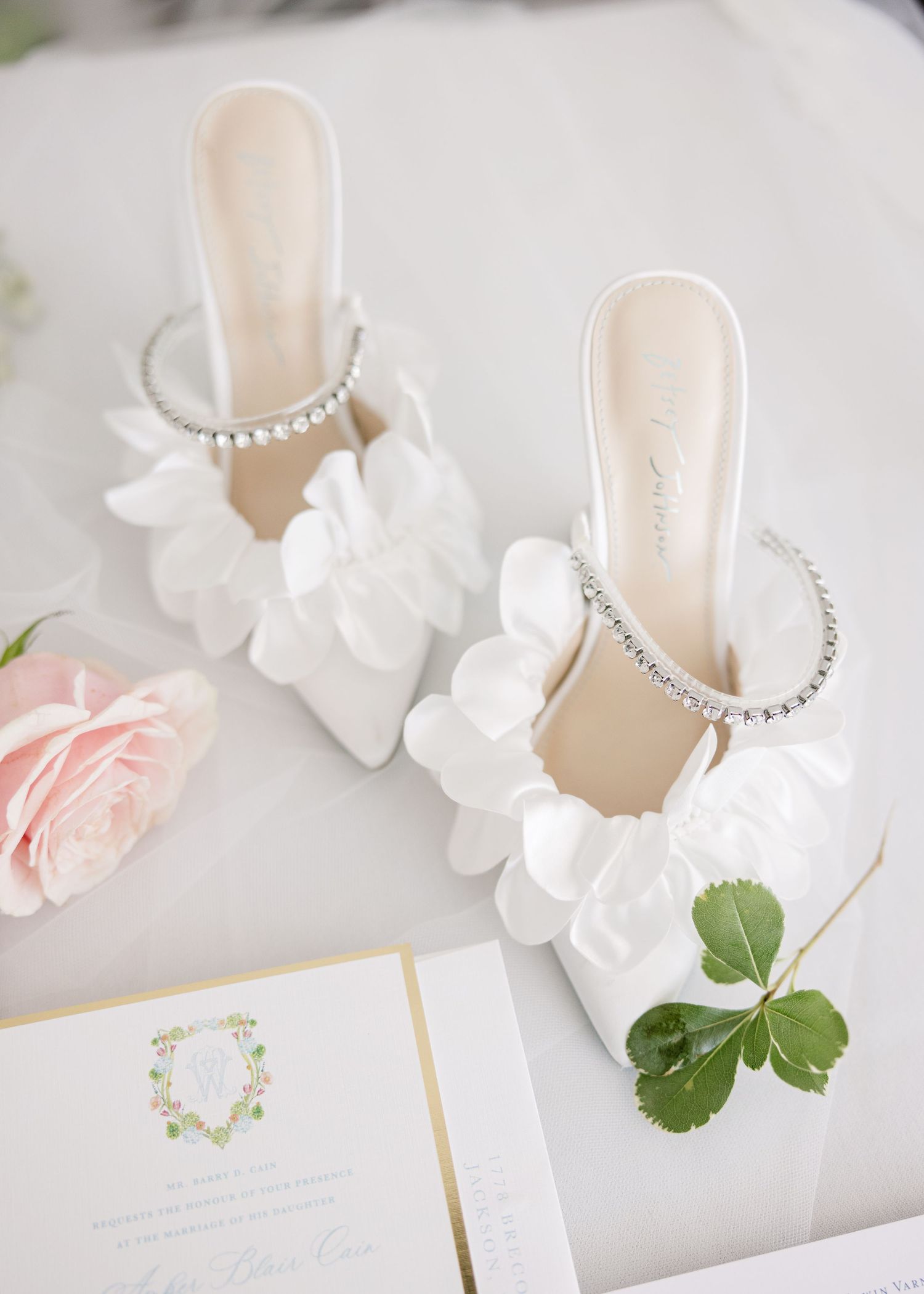 Wedding flat lay with elegant white shoes, flowers and stationery on light background.