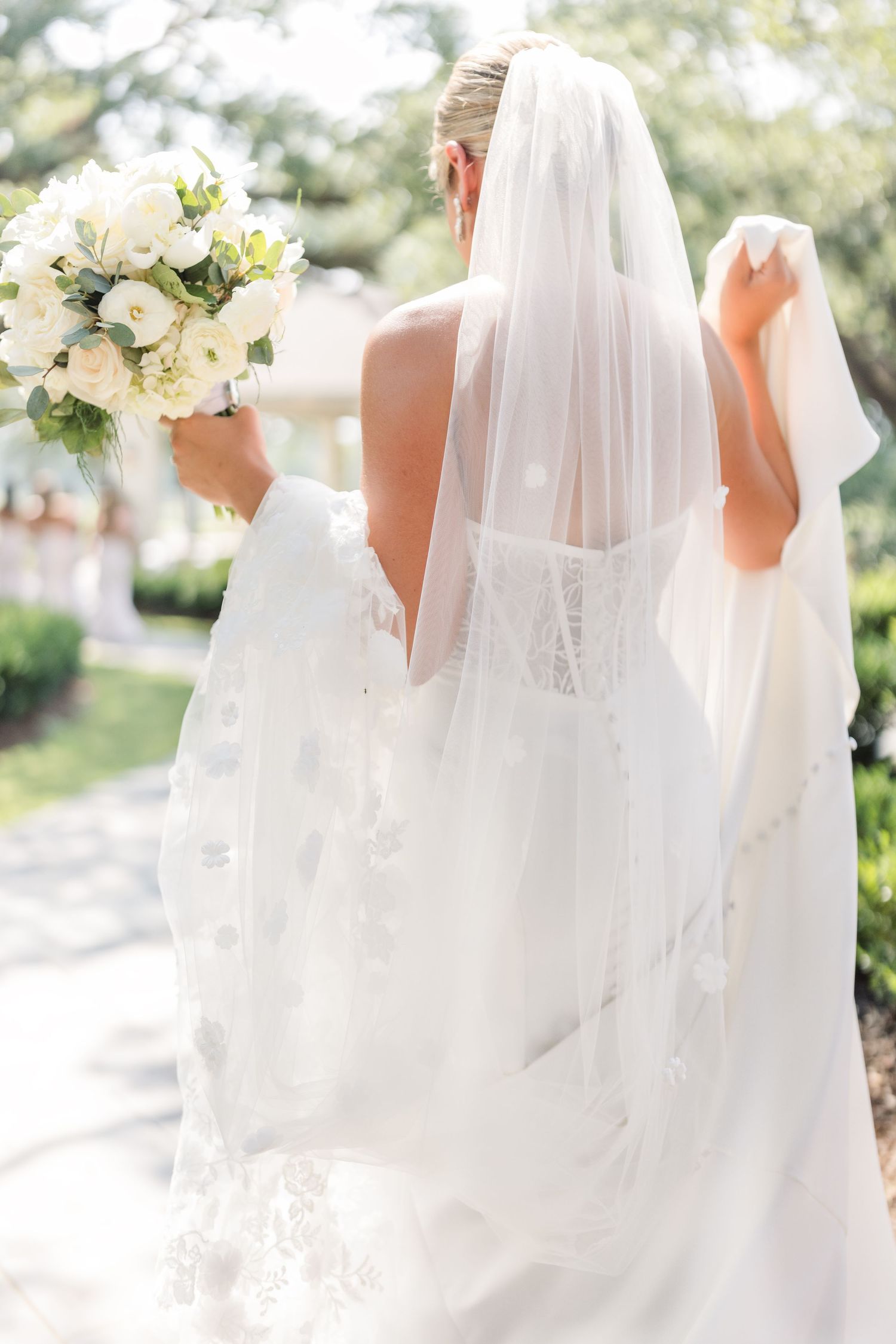 Row of white wedding dresses with flowing veils captured in natural outdoor lighting.