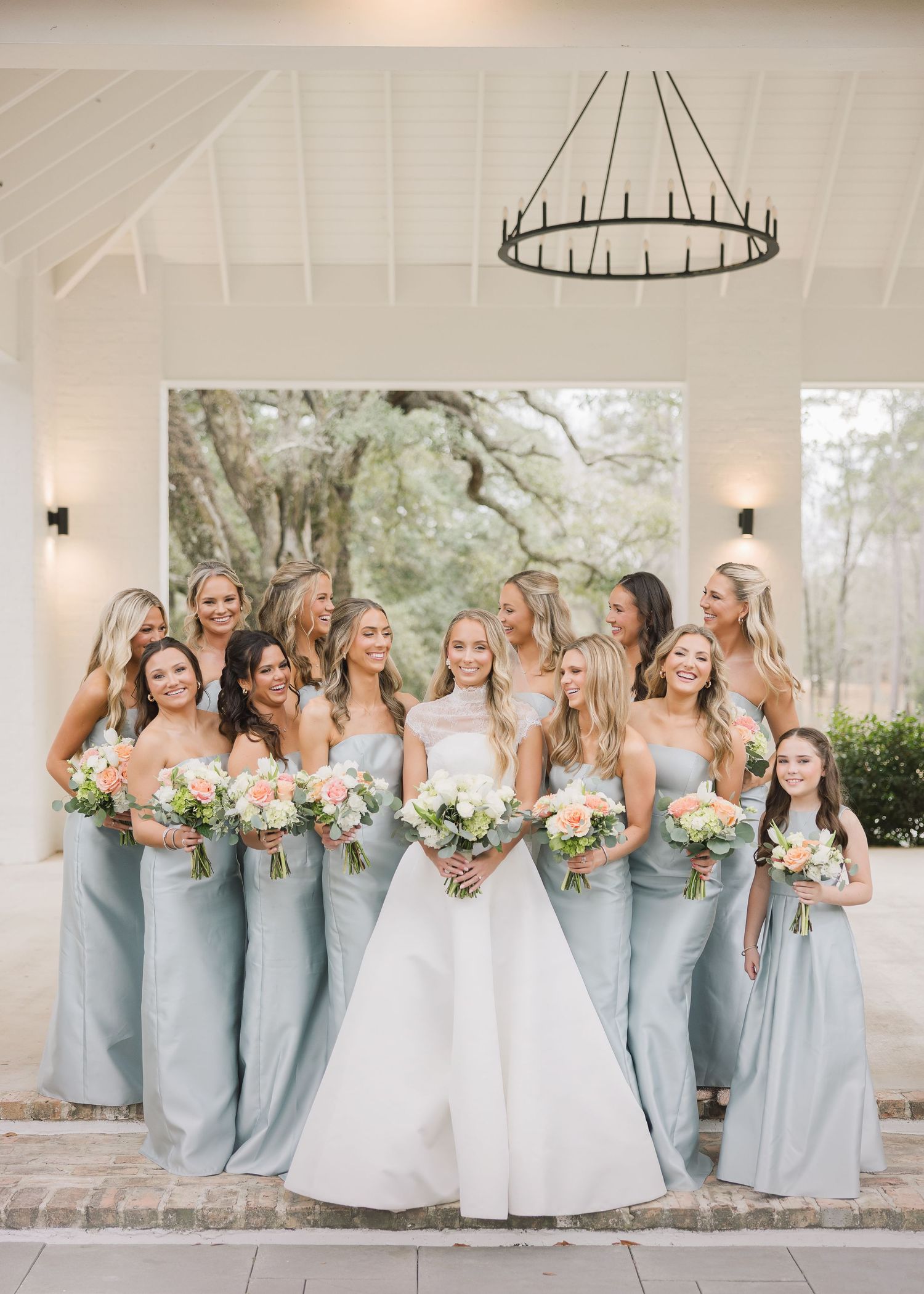A group in light blue bridesmaid dresses and white wedding gowns pose together for a fun outdoor photo series.