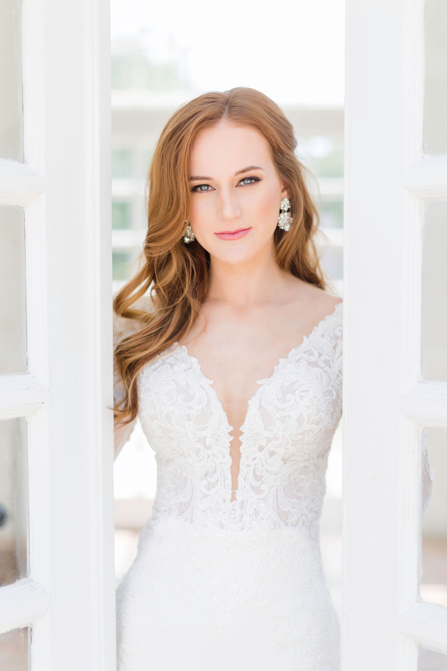 Delicate lace wedding gown with plunging neckline photographed against white architectural details.