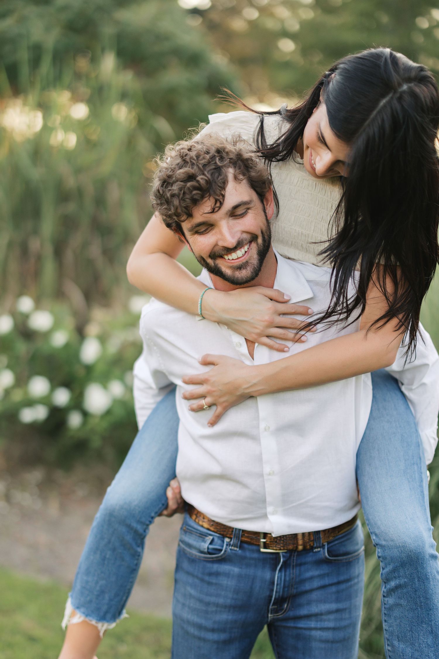 A joyful piggyback ride between a couple outdoors with natural bokeh lighting in the background.