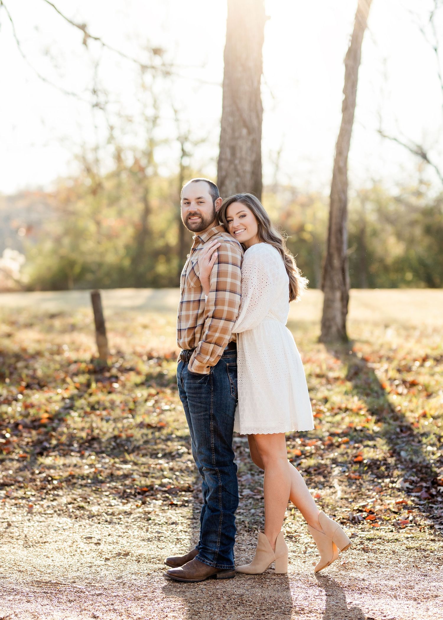 Couple embracing in sunlit autumn forest setting with fallen leaves.