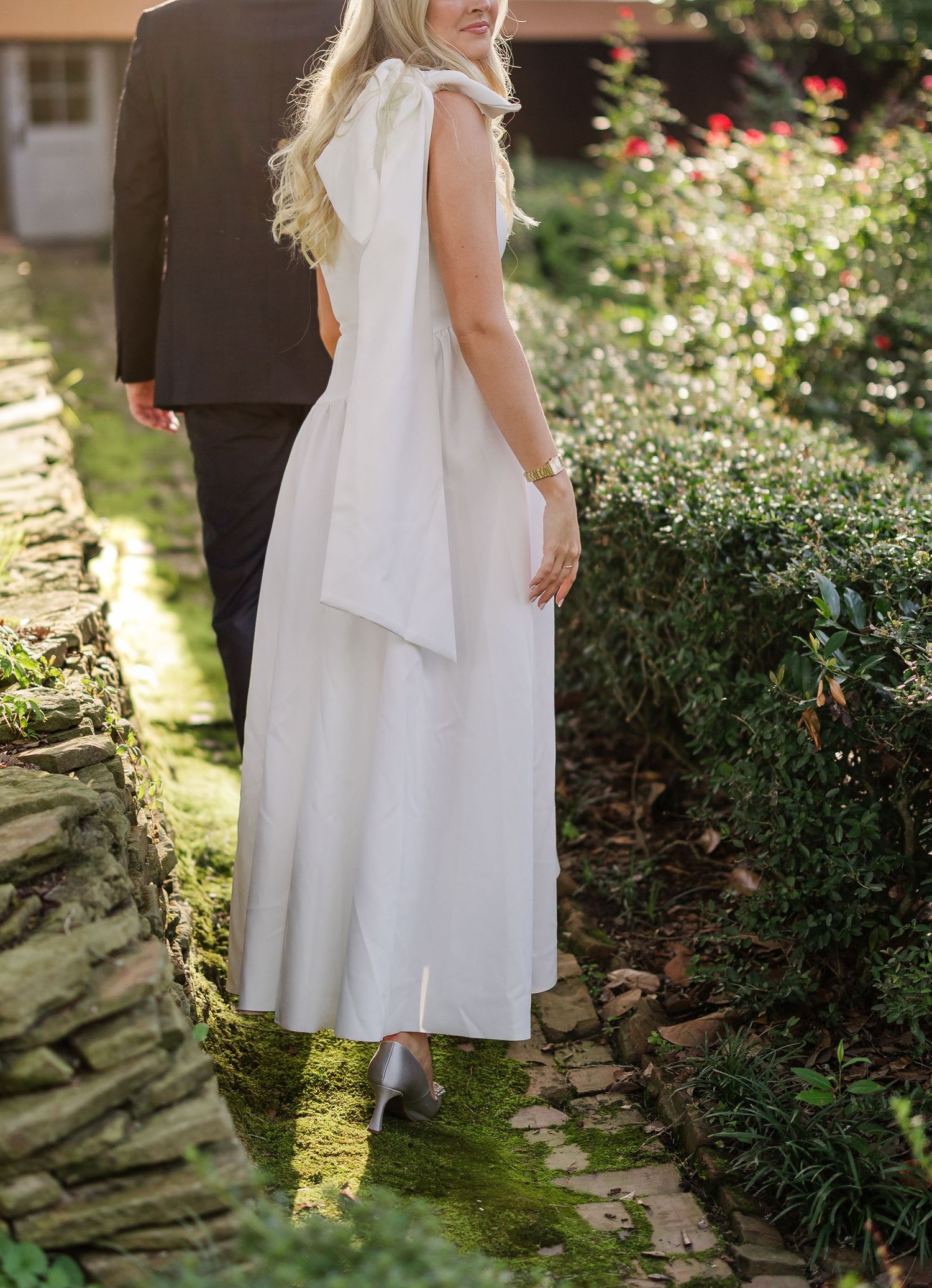 White dress flowing in a garden setting with stone pathway and lush greenery.