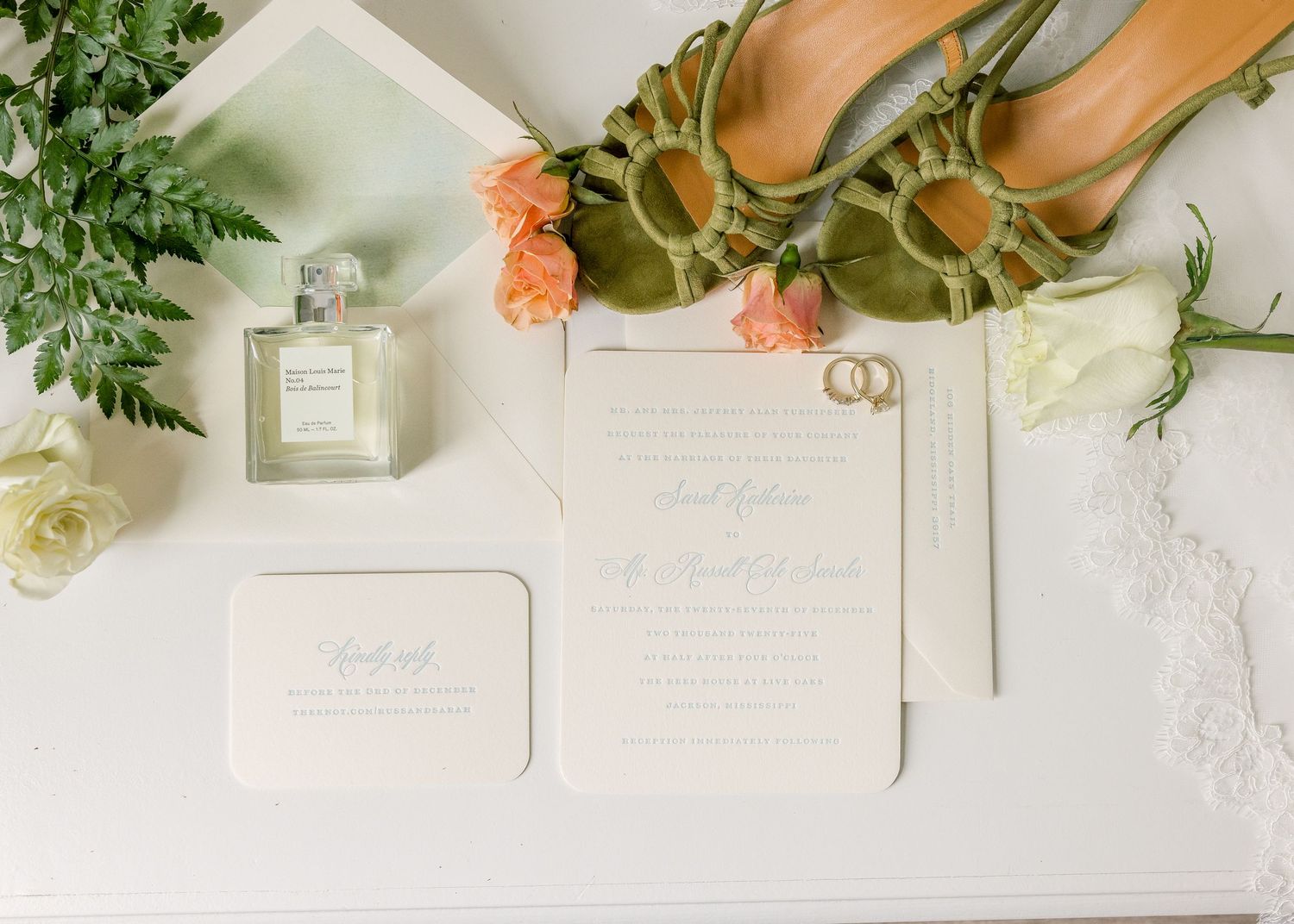 Wedding stationery and floral decorations arranged on white linen with delicate greenery and peach-colored roses.