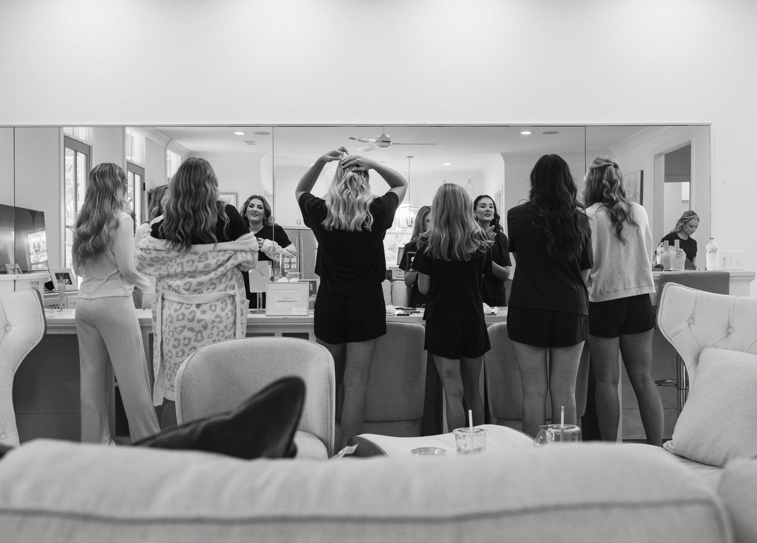 A black and white photograph shows a group of people standing at a counter with mirrors in what appears to be a salon.