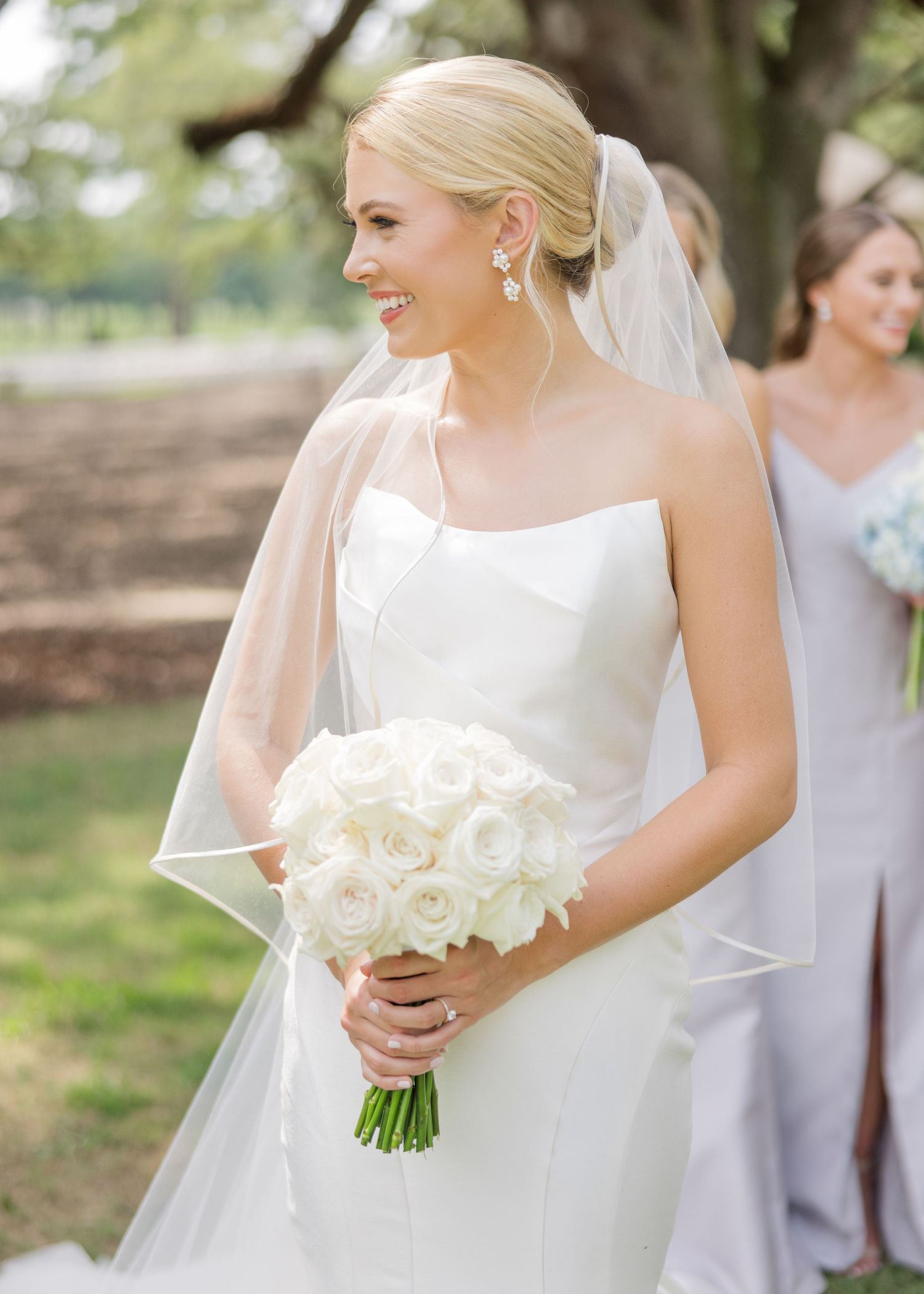 Bride in classic white gown holding elegant white rose bouquet outdoors.