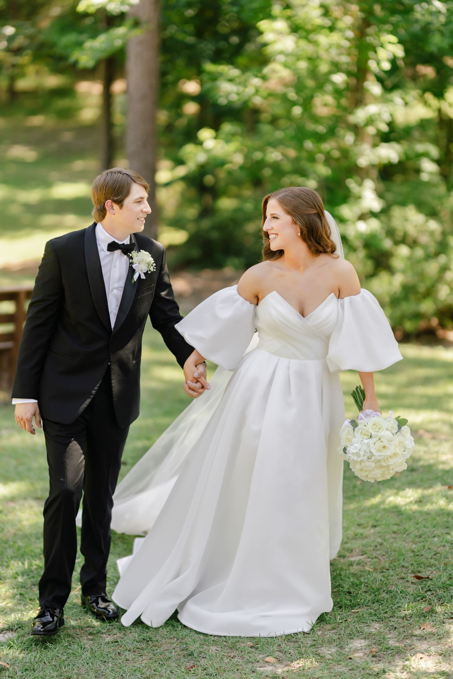 Playful wedding couple interacts on grassy lawn in formal attire.
