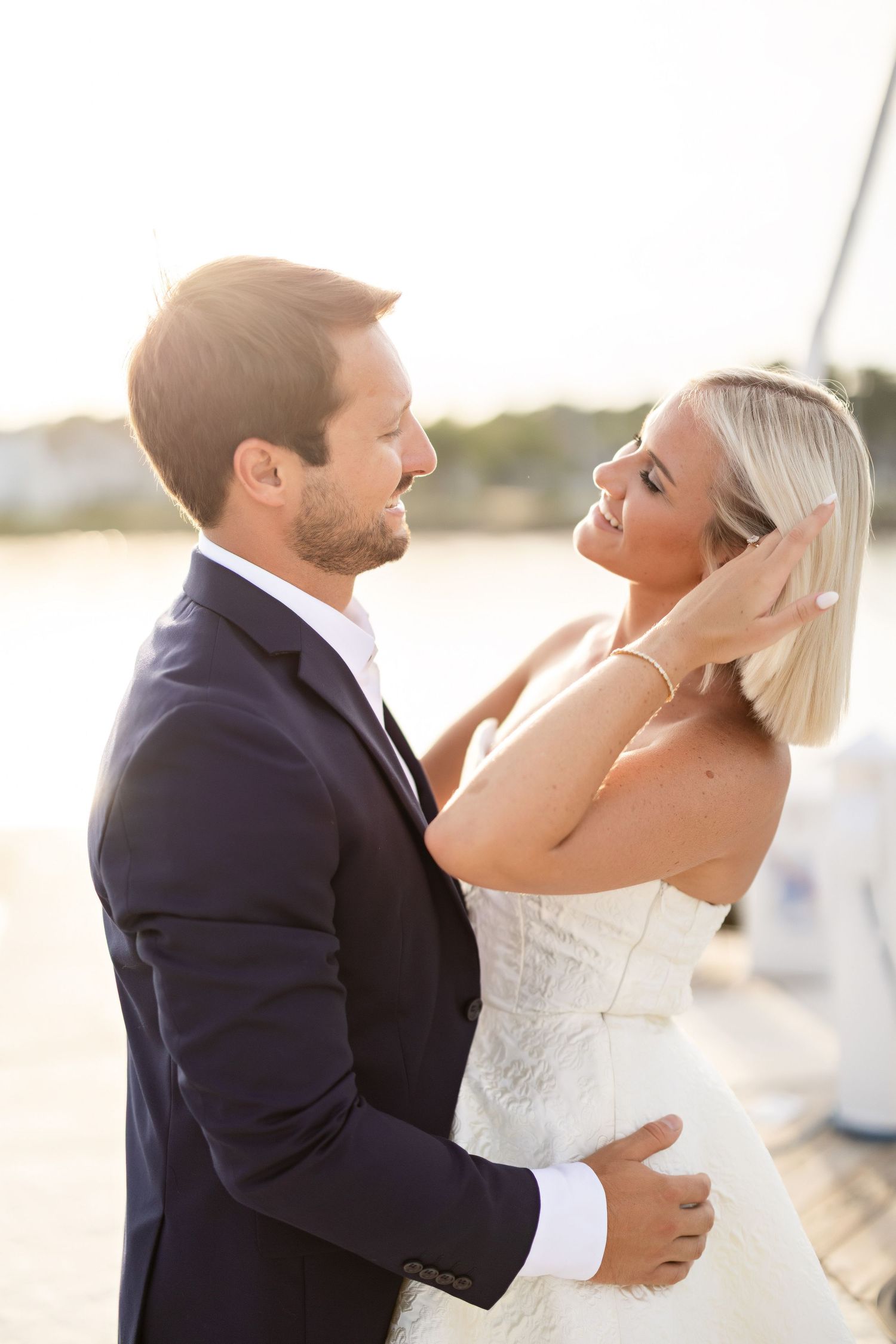 Couple in formal attire sharing romantic moments by waterfront at sunset.