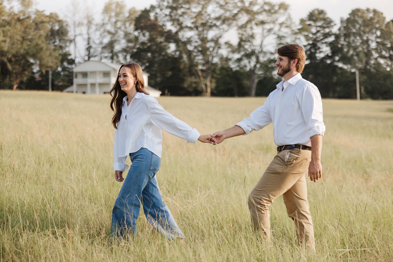 Playful moment in a golden field with casual white shirts and denim.