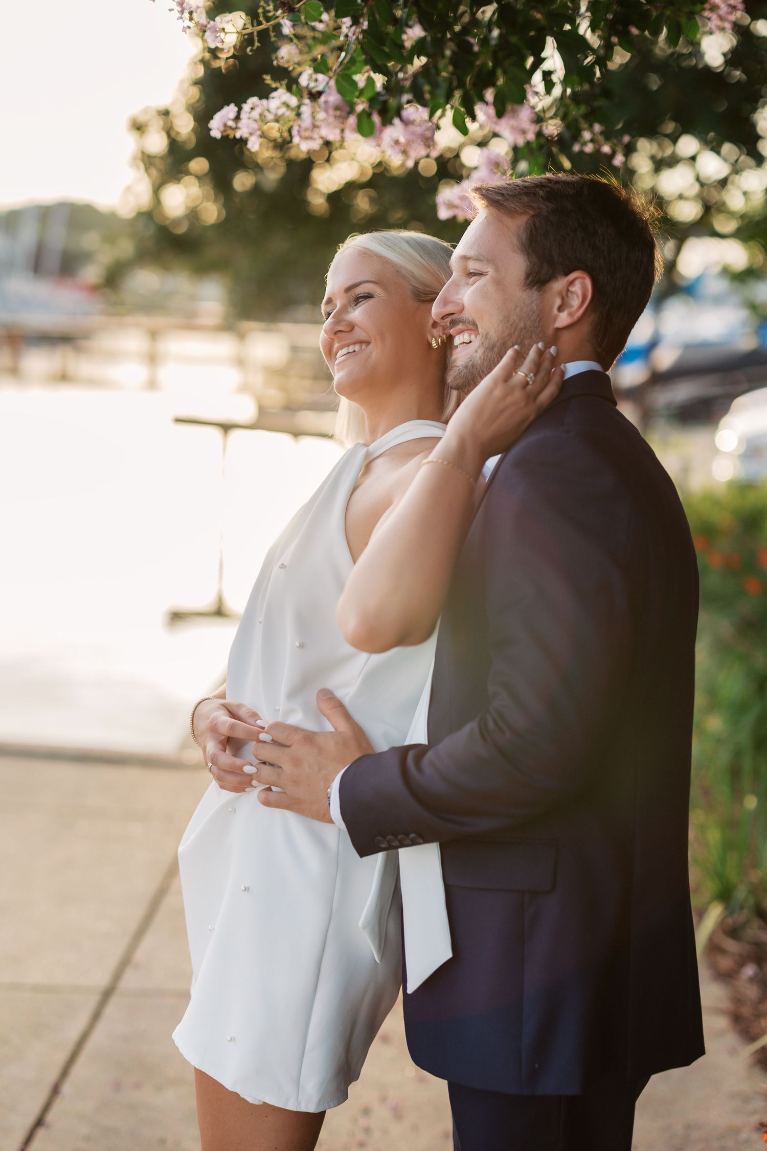 A couple shares a romantic moment at sunset in formal attire against a blurred natural background.