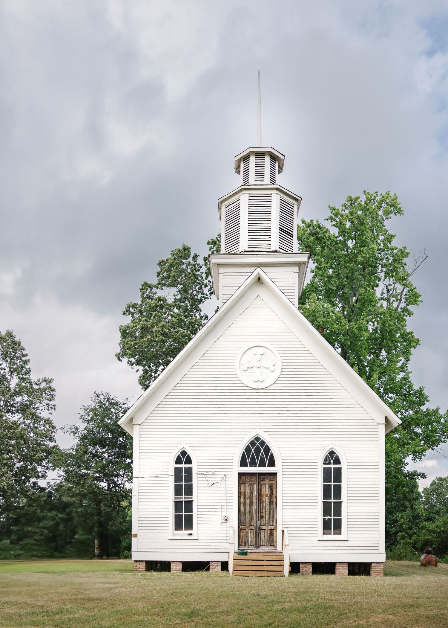 A historic white wooden church with arched windows and a bell tower shown from different angles on a grassy hillside.