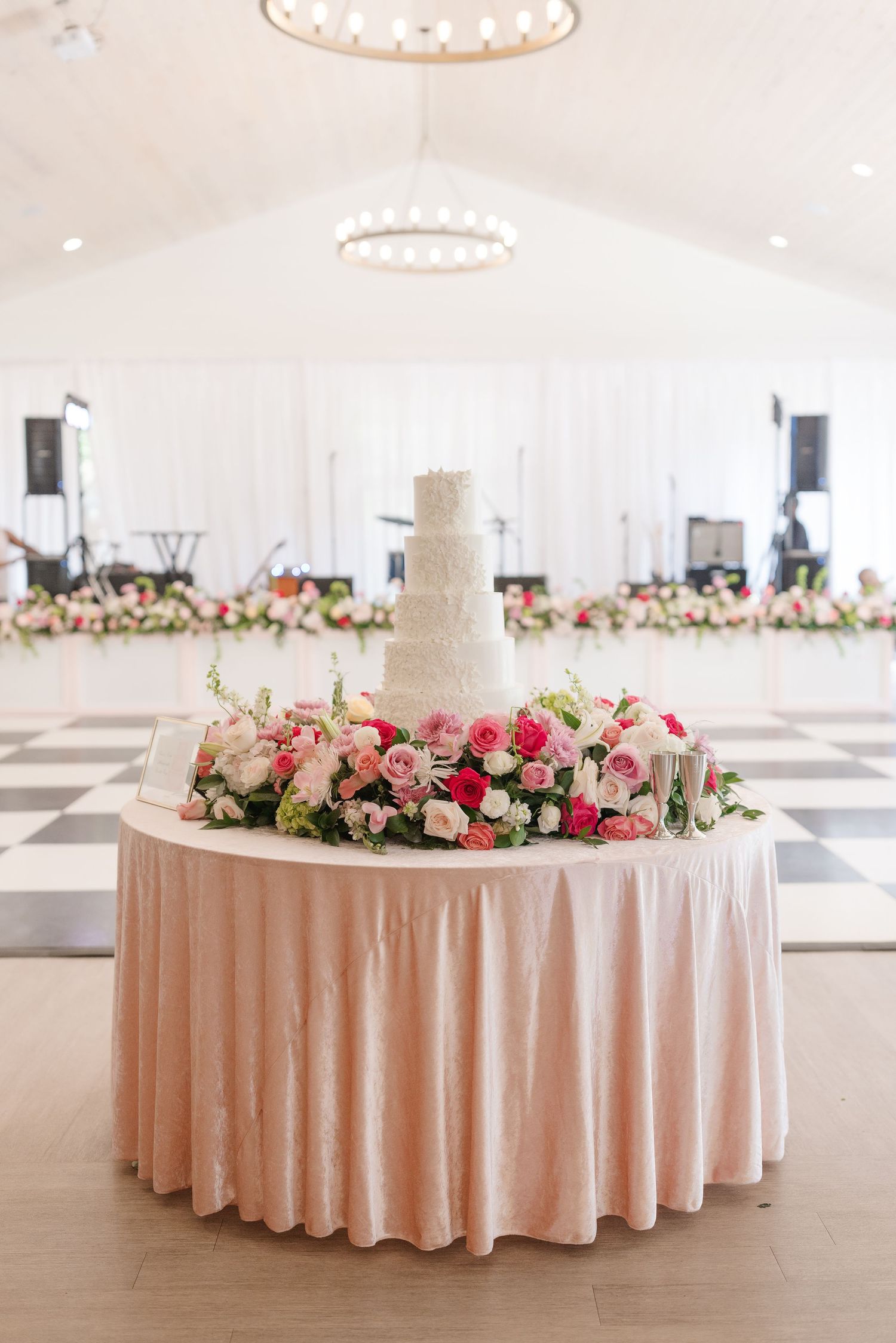 Large round tables with blush pink linens and floral centerpieces in an elegant white wedding reception tent.