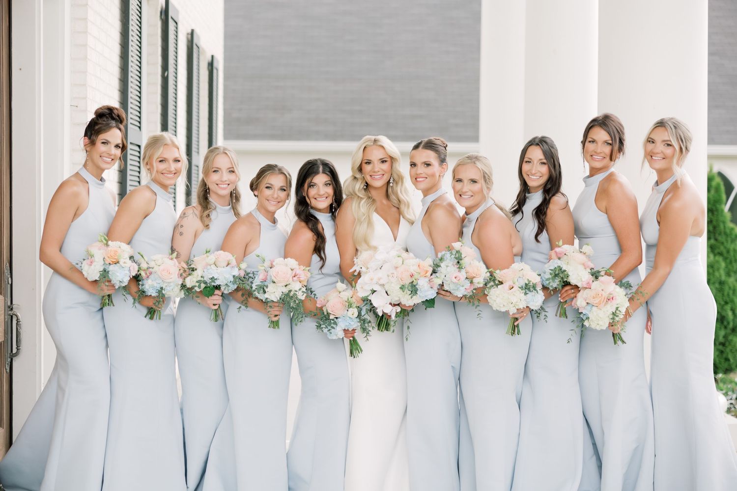 Bridesmaids in light blue dresses holding white floral bouquets pose for wedding photos.