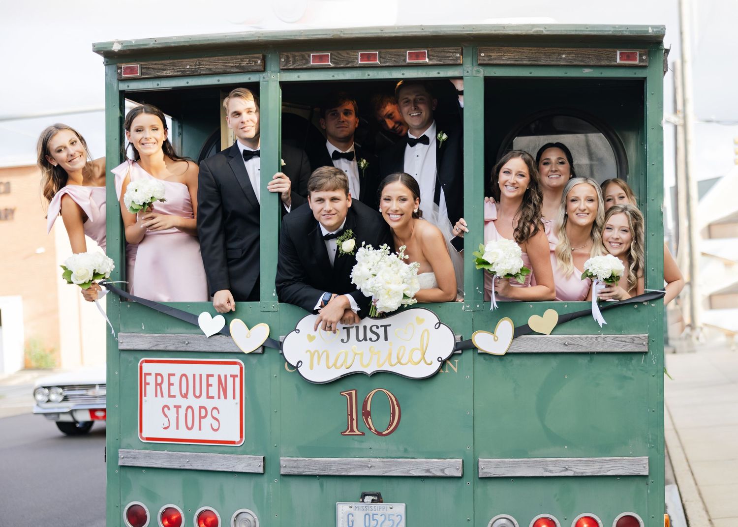 Guests peek out of a vintage green trolley car on a sunny day.