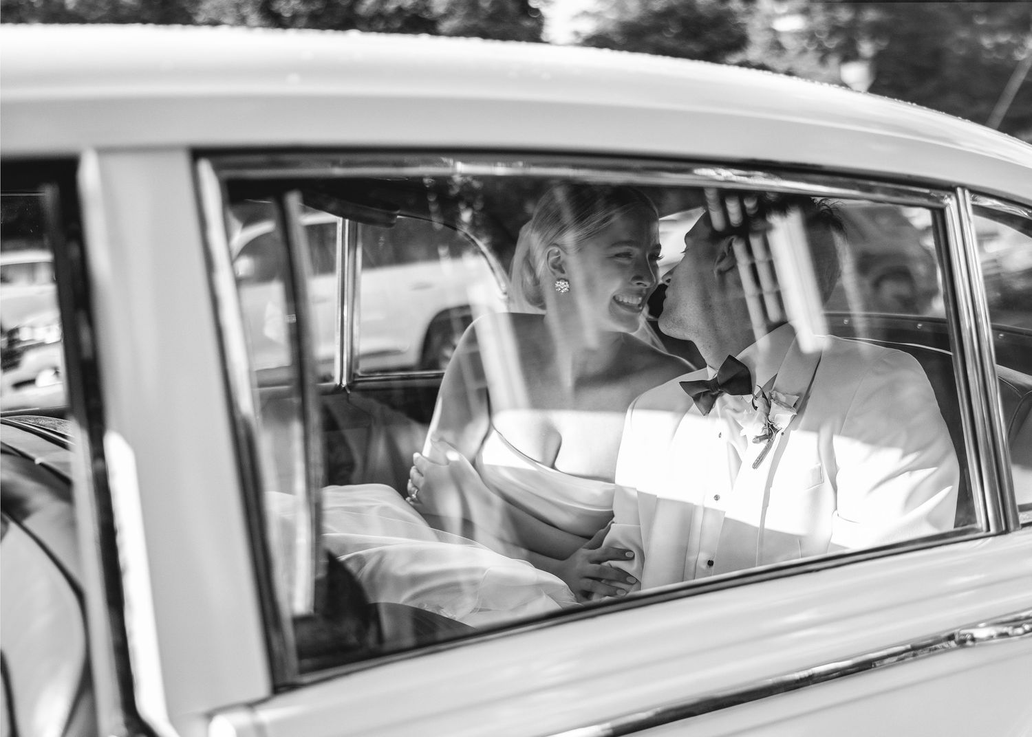 Black and white photo of couple in vintage car on wedding day.