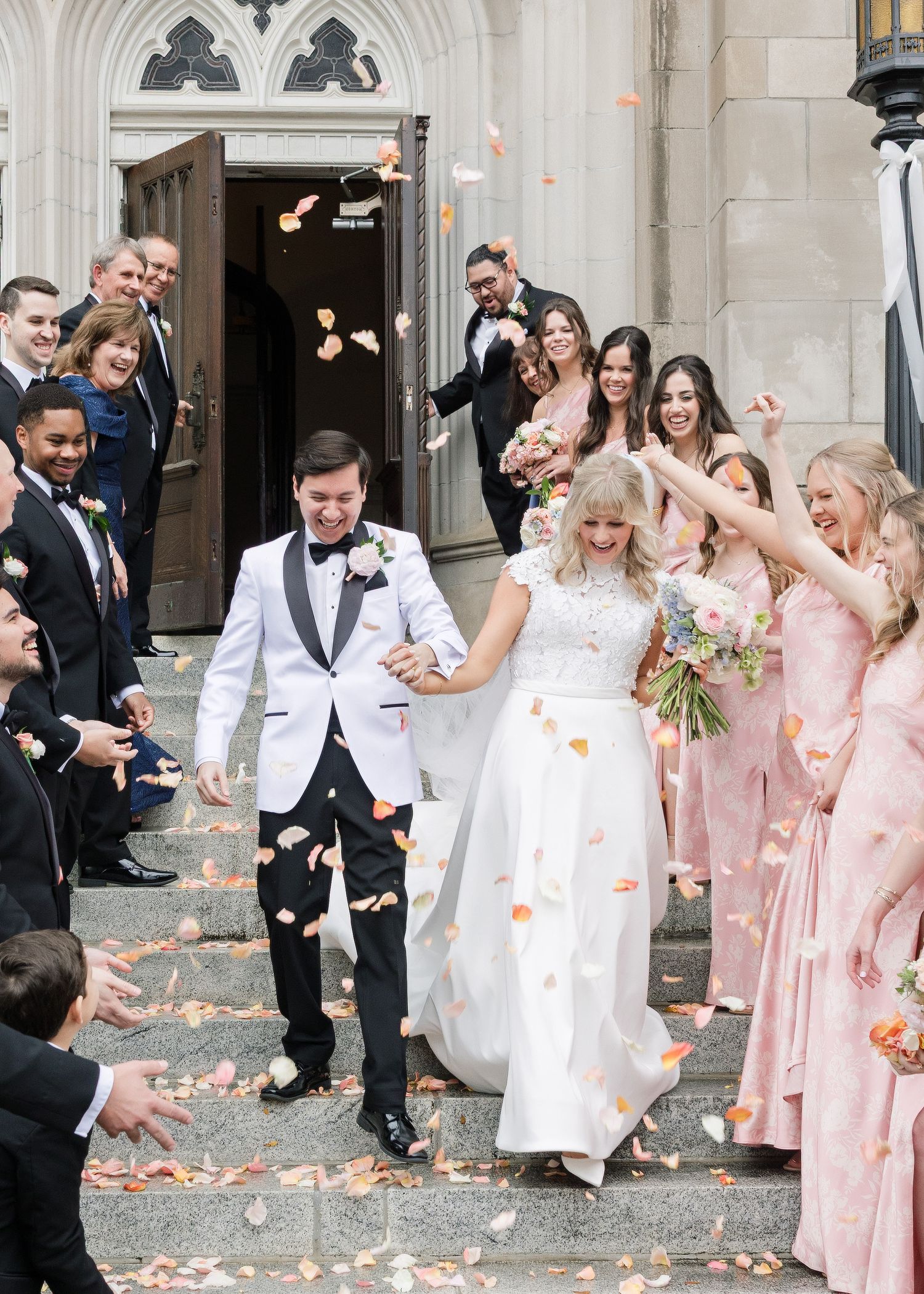 Wedding party celebration with flower petals being tossed outside a grand church entrance.
