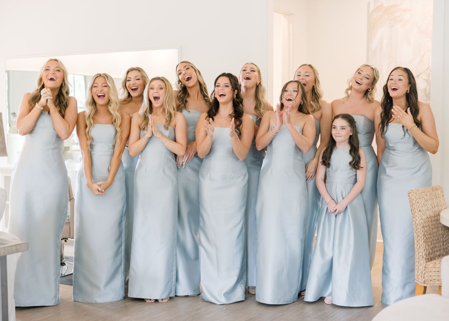 A group in matching light blue floor-length bridesmaid dresses pose together while making playful expressions.
