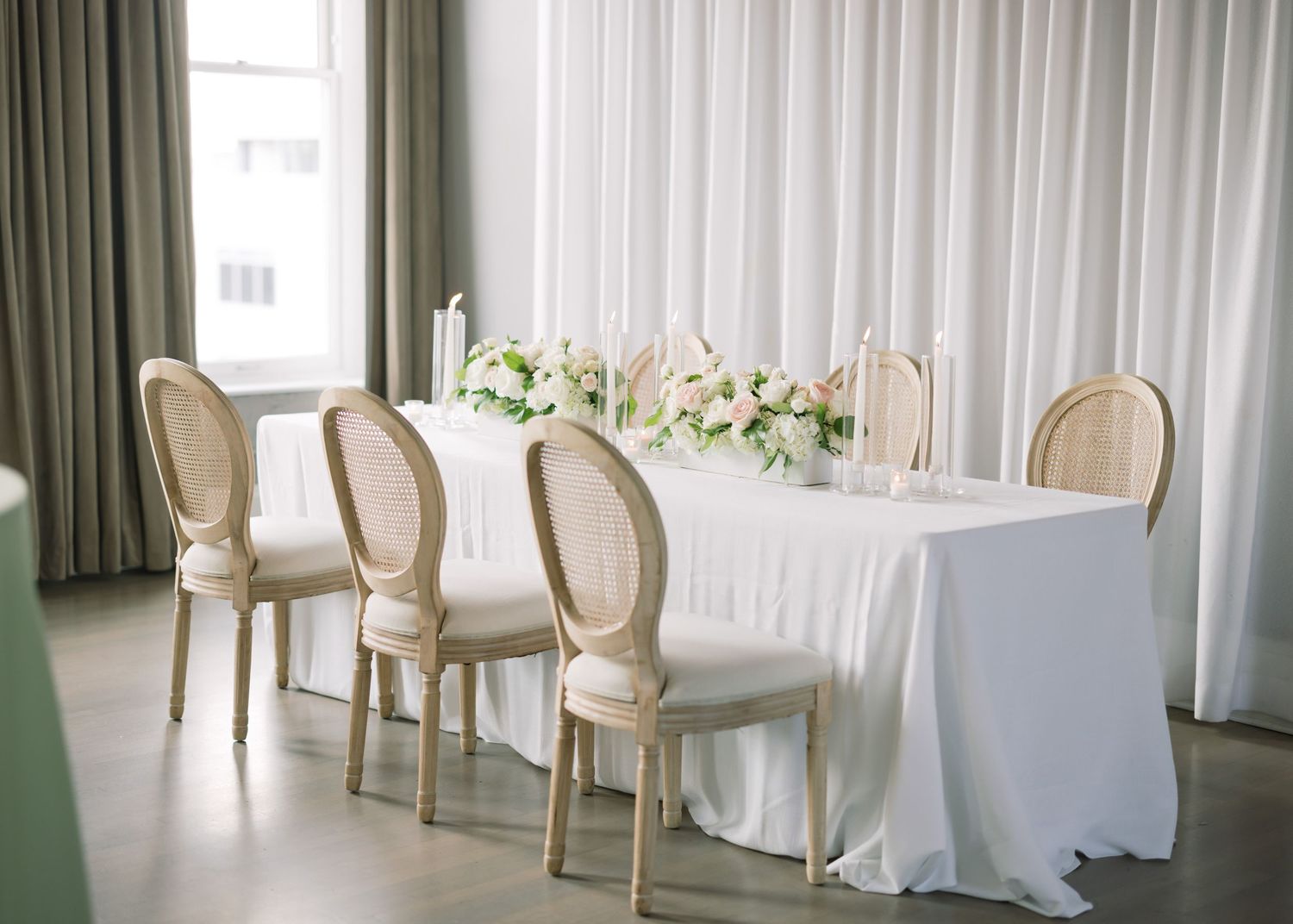 Elegant wedding reception table setup with white linens and pale pink floral centerpieces.