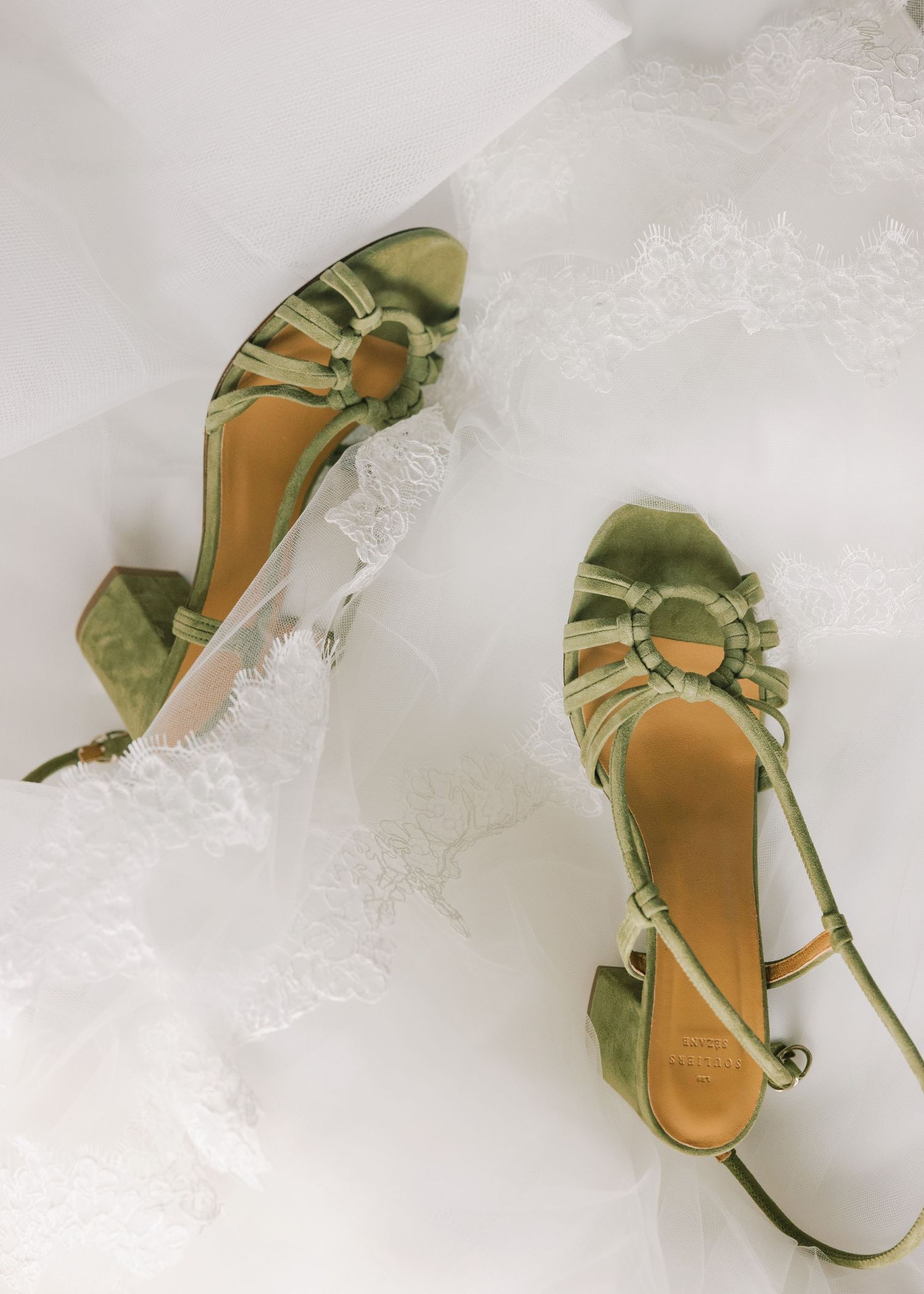 Elegant mint green satin bridal shoes with delicate bow details arranged in a row against a white lace background.